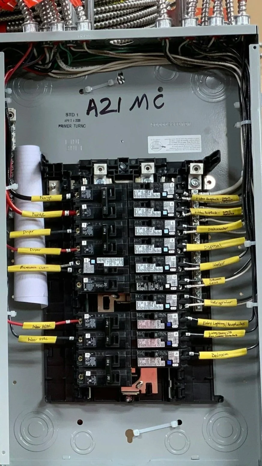 Electrical panel with breaker switches, labeled yellow wiring for different rooms and appliances, handwritten notes, and multiple wires connected.