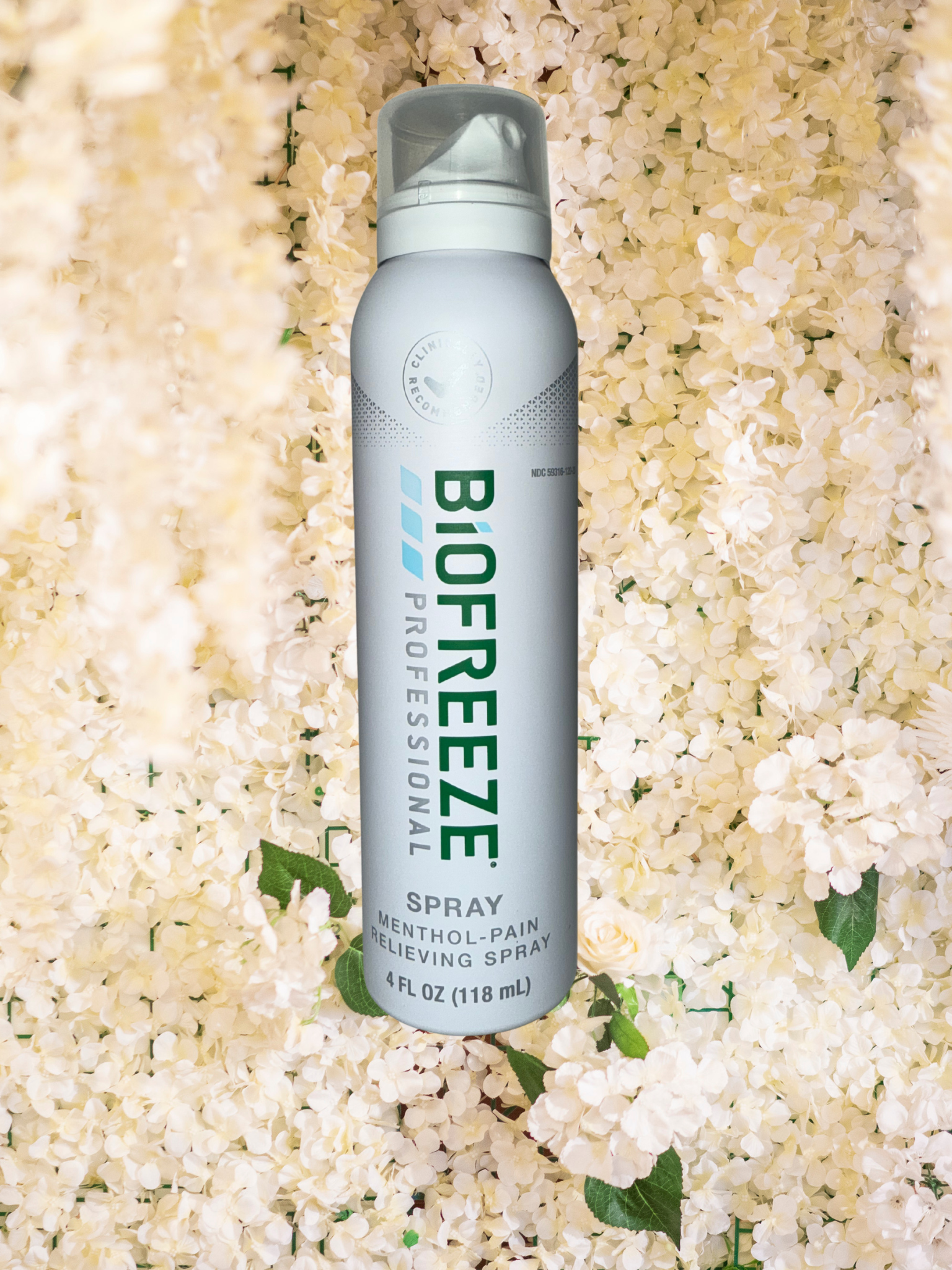 A 4 fluid ounce (118 mL) bottle of Biofreeze Professional menthol pain relieving spray with a white background and floral surroundings.