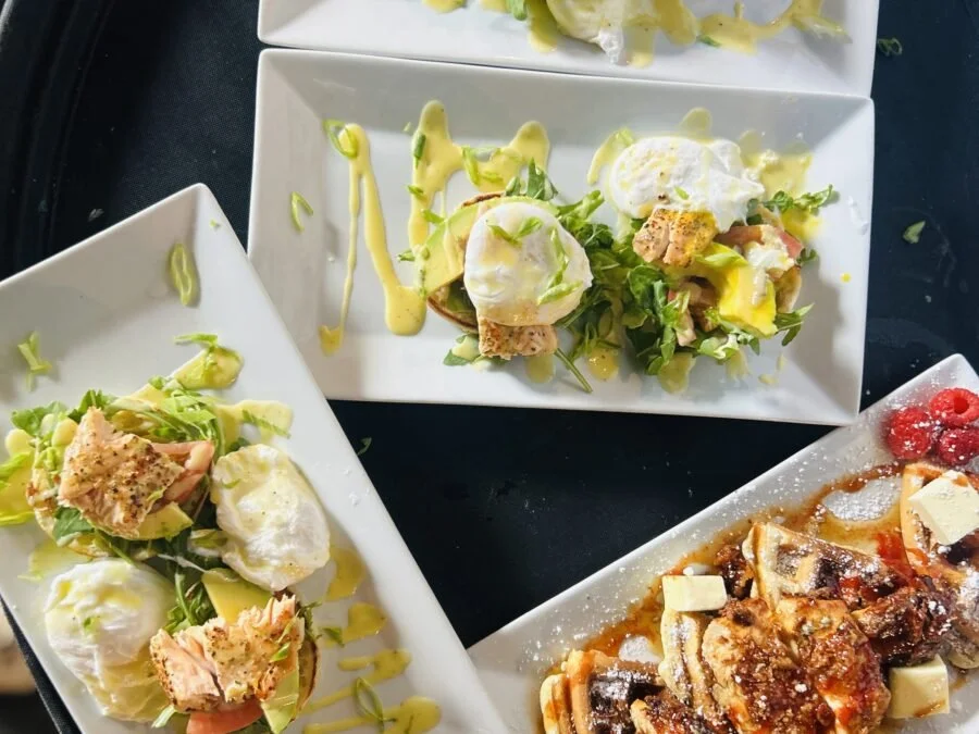 Three plates of food on a black table with various salads and a baked eggplant dish on the bottom right plate.