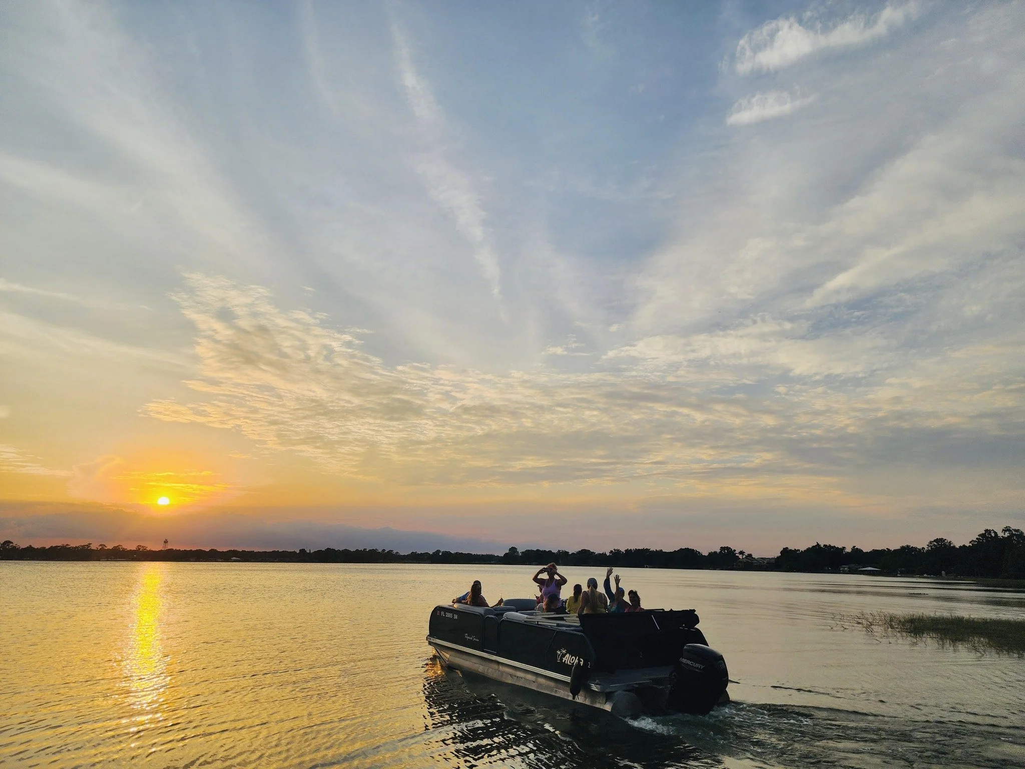 A group of people on a boat enjoying a sunset over a body of water, with partly cloudy sky.