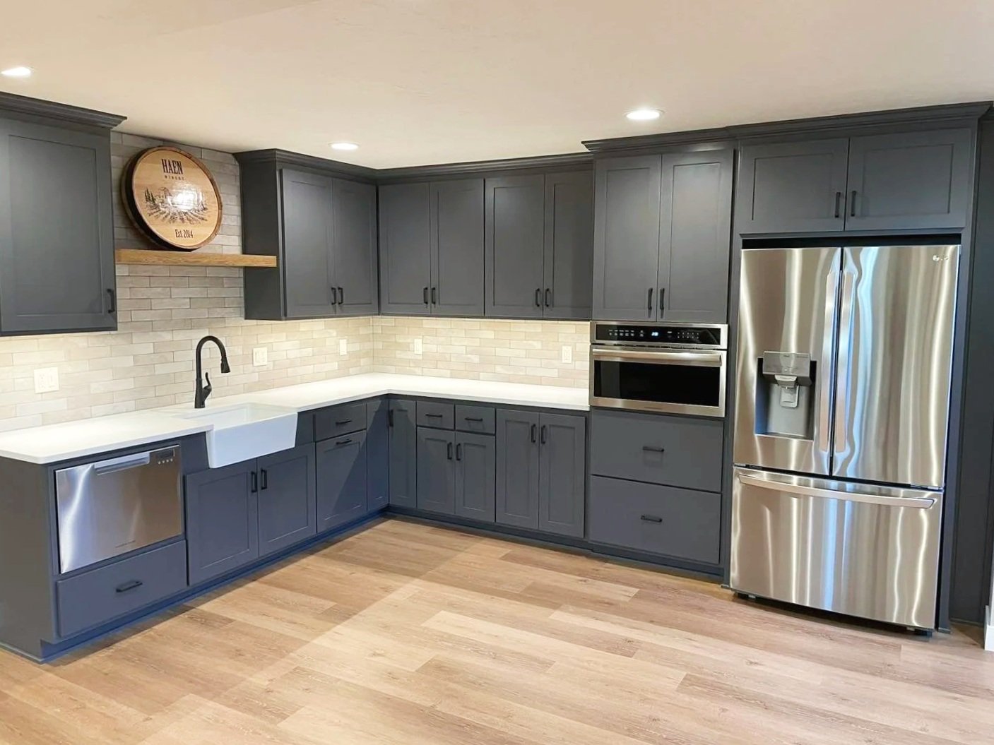 Photo of a kitchen renovation by Revival Homes WI, featuring dark blue cabinets, custom backsplash, farmhouse sink, and modern stainless steel appliances.