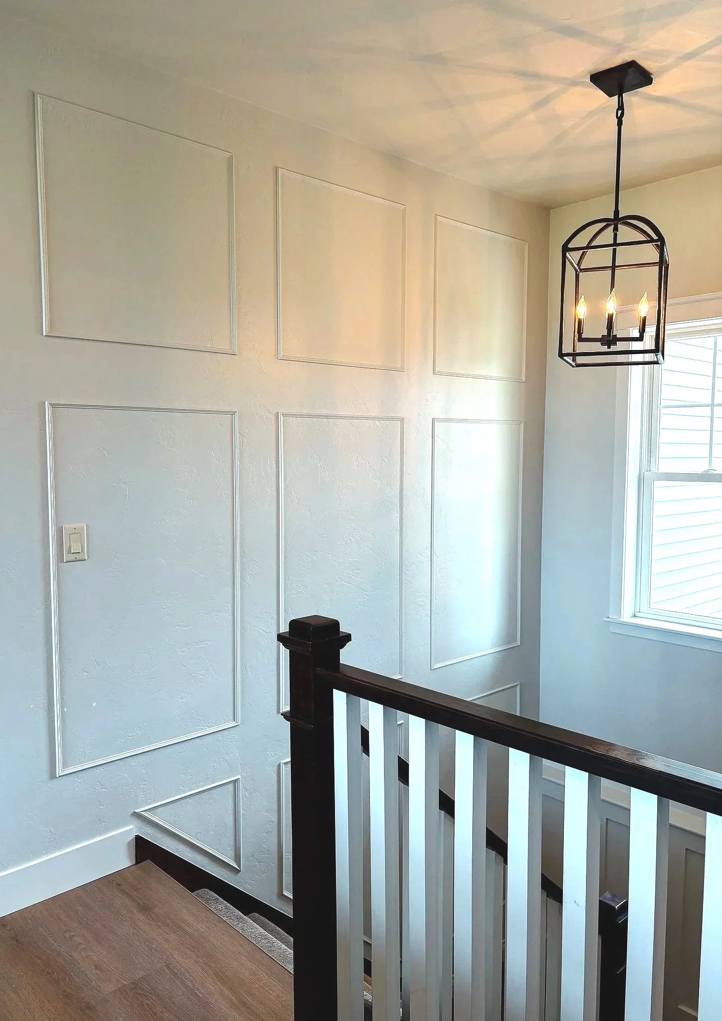 Photo of a beautiful, bright stairwell in a classic home with rustic lighting and decorative wall trim created by Revival Homes.