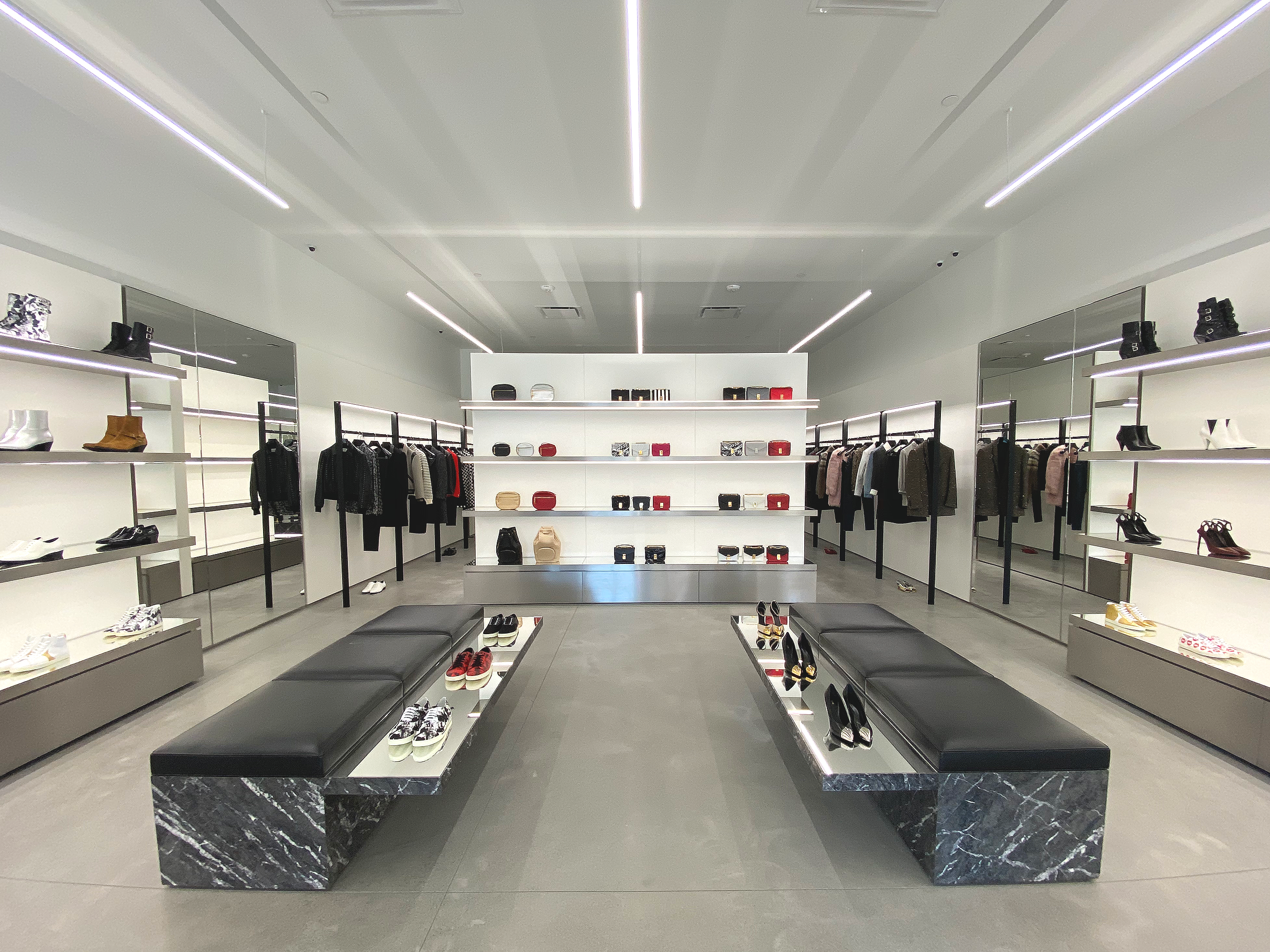 A modern, minimalistic clothing store with shoes, handbags, and apparel on display, featuring sleek black and white decor and mirrored walls.