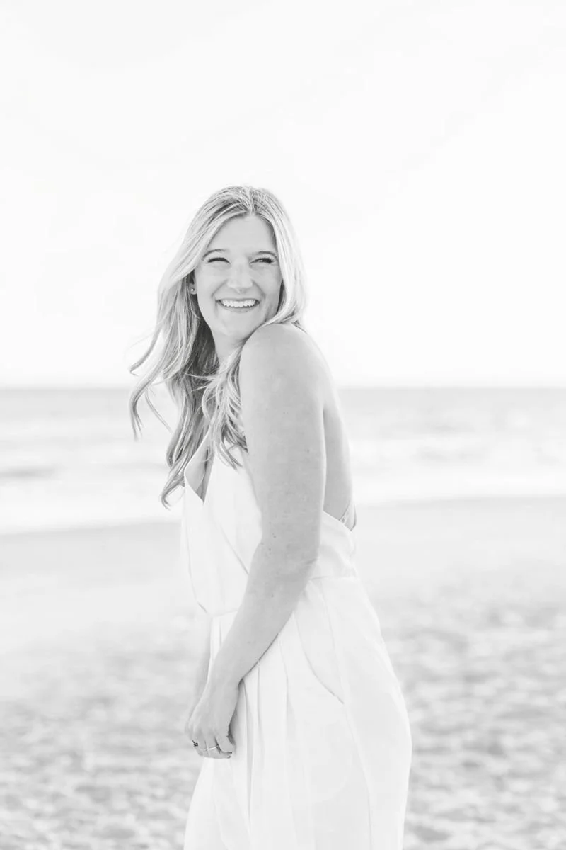 Woman smiling and laughing on a beach, wearing a light-colored dress