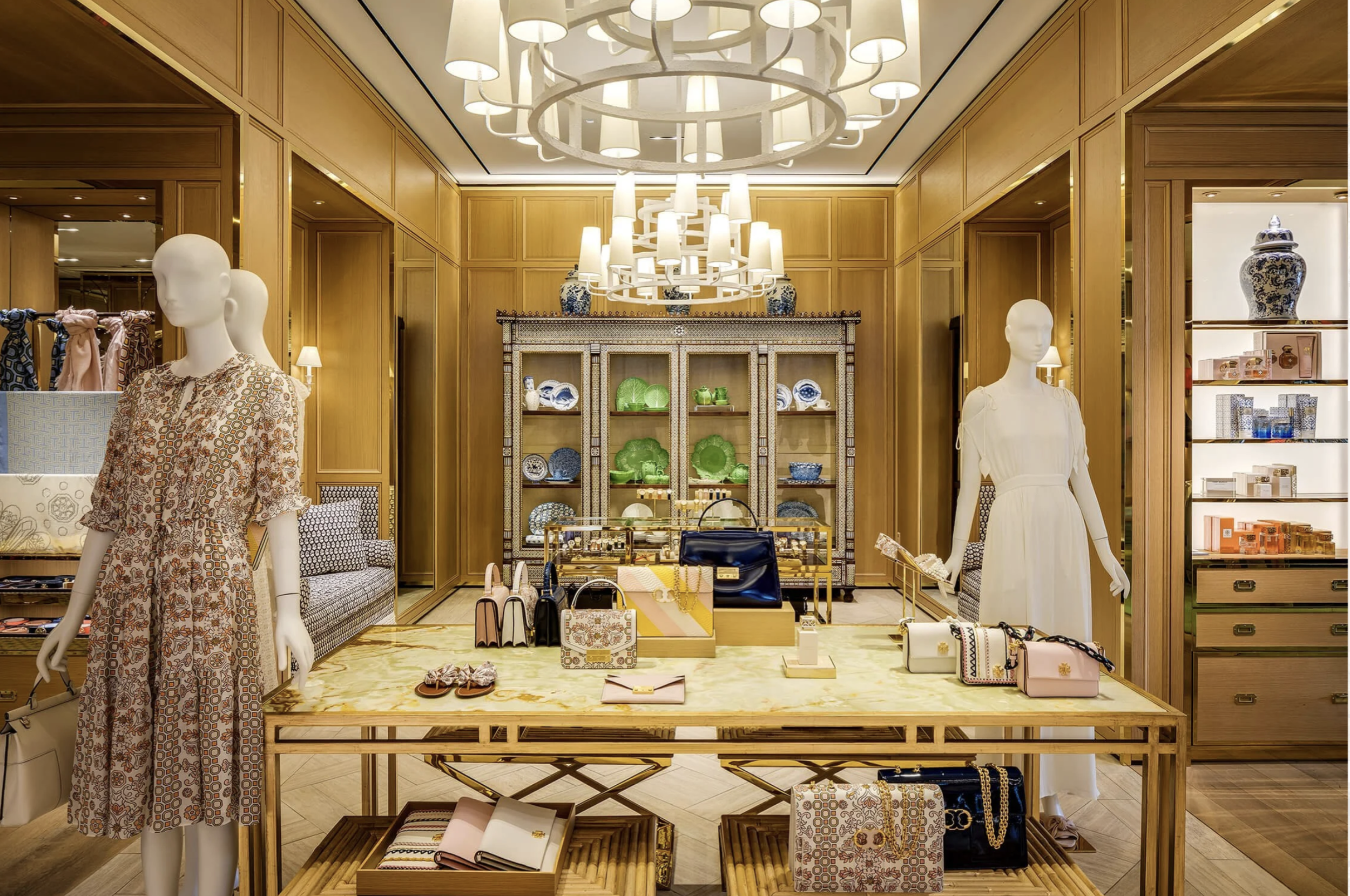 Interior of a luxury retail store displaying girls' clothing, handbags, and accessories with wooden walls, mannequins, and decorative shelving.