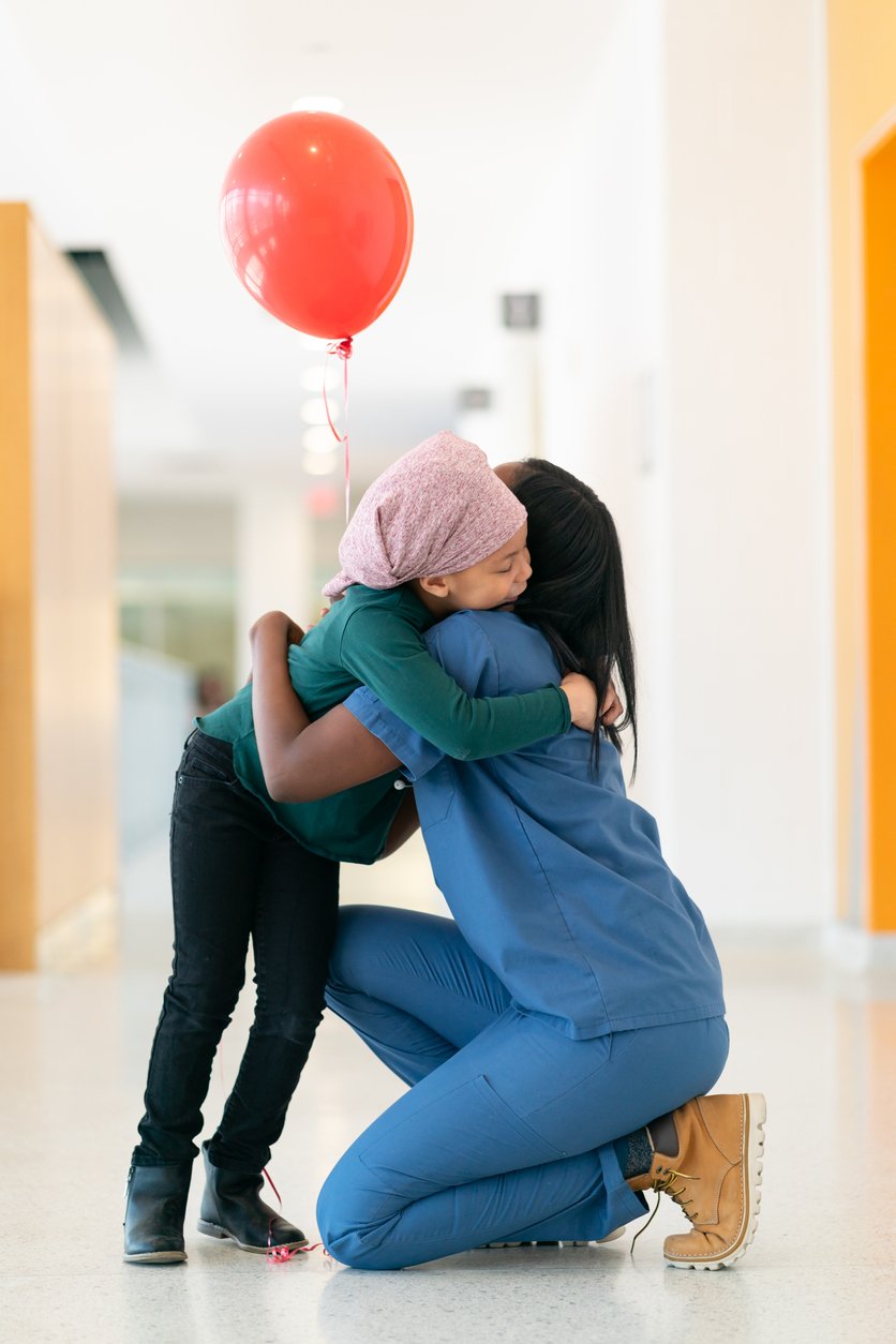 Child comforted by her nurse in a hospital corridor, representing the medical challenges Camino Pediatric helps families navigate.