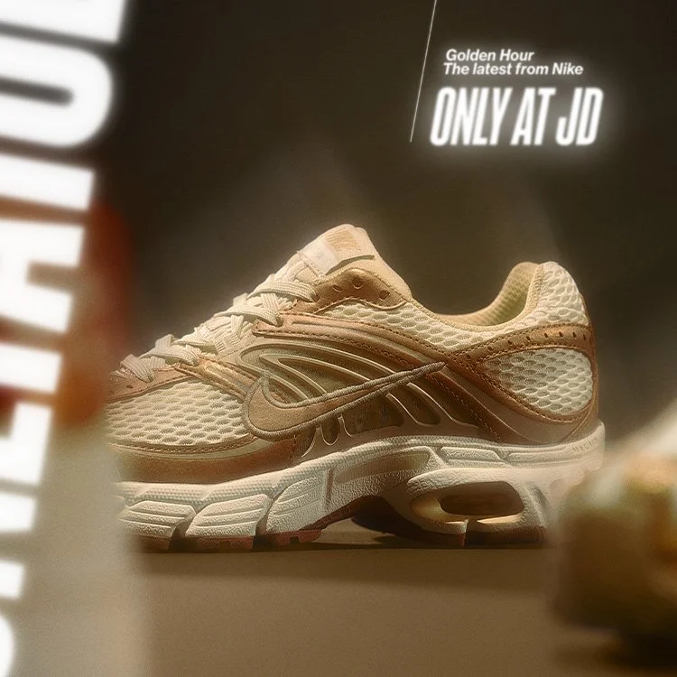 A beige Nike sneaker on display with a sign that reads 'Golden Hour The latest from Nike ONLY AT JD' in the background.