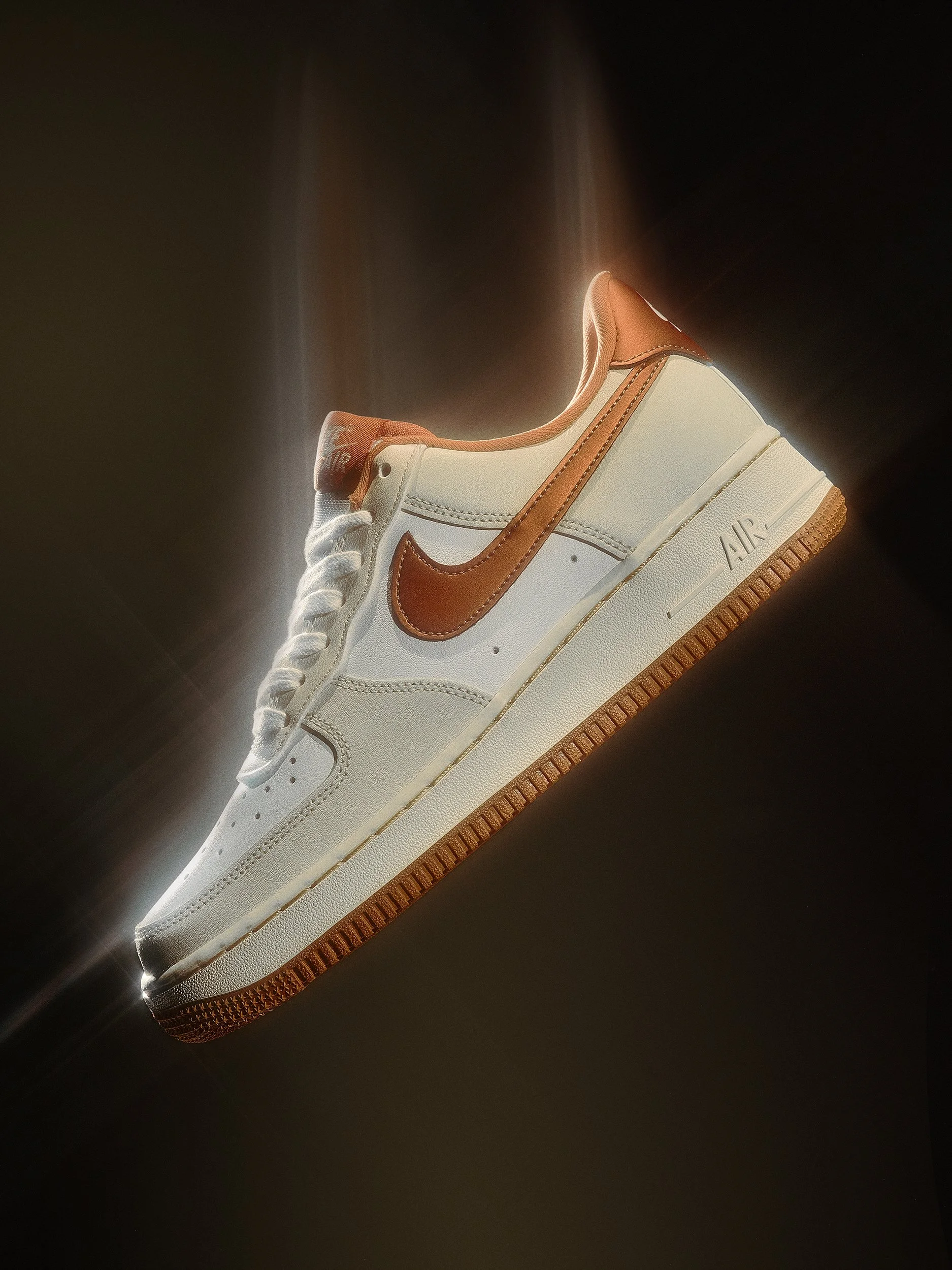 A white Nike Air Force 1 sneaker with brown Nike swoosh logo floating against a dark background with light effects.