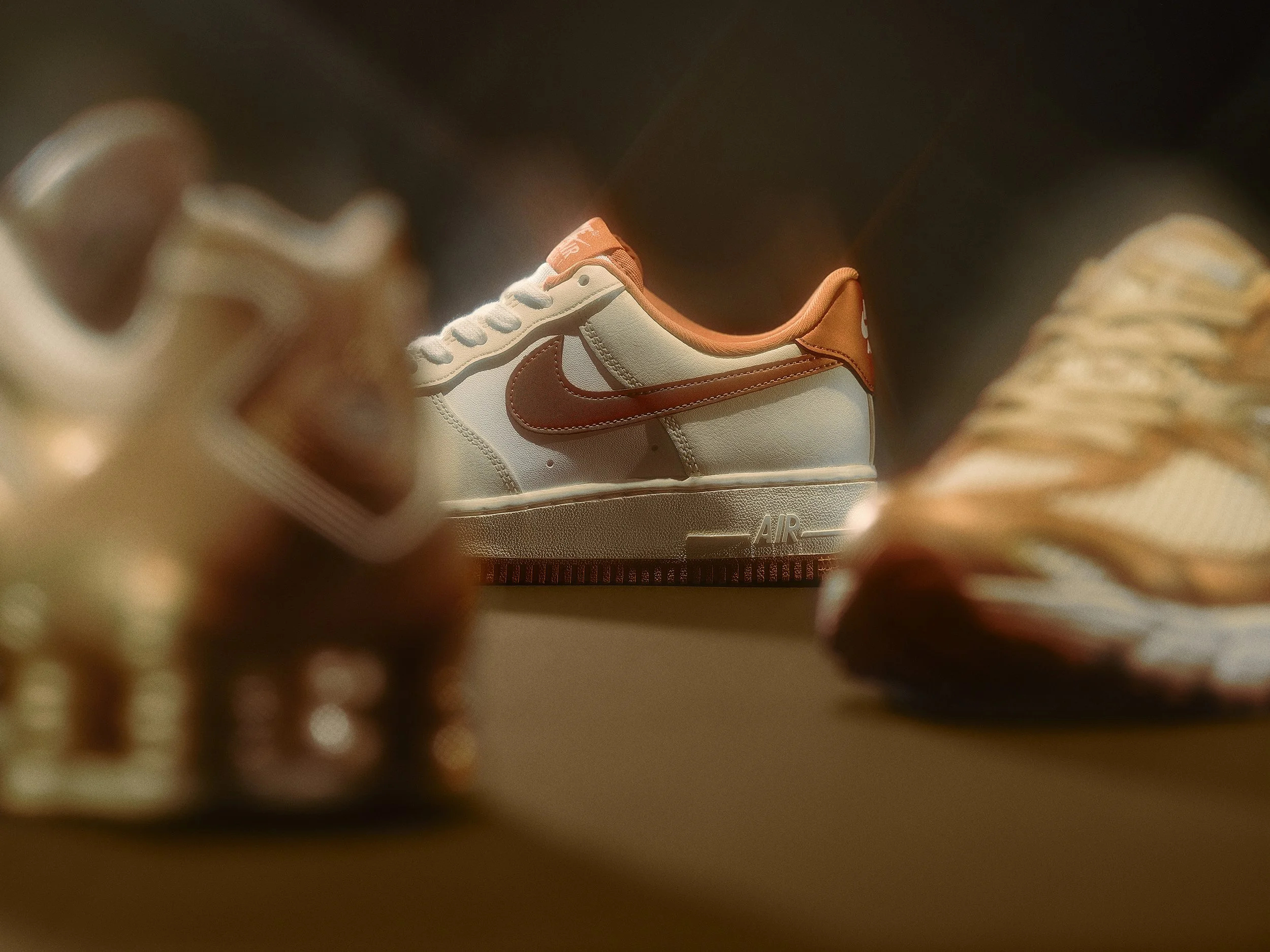 A pair of Nike sneakers with beige and brown colors, focus on the back of one shoe in the center, with other shoes slightly out of focus on either side.