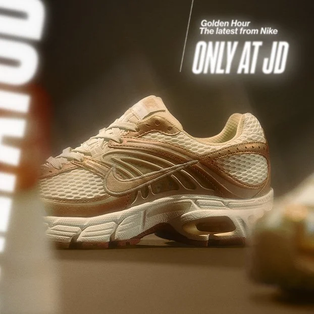 A beige and brown Nike sneaker showcased on display with a sign above it reading "Golden Hour The latest from Nike ONLY AT JD."