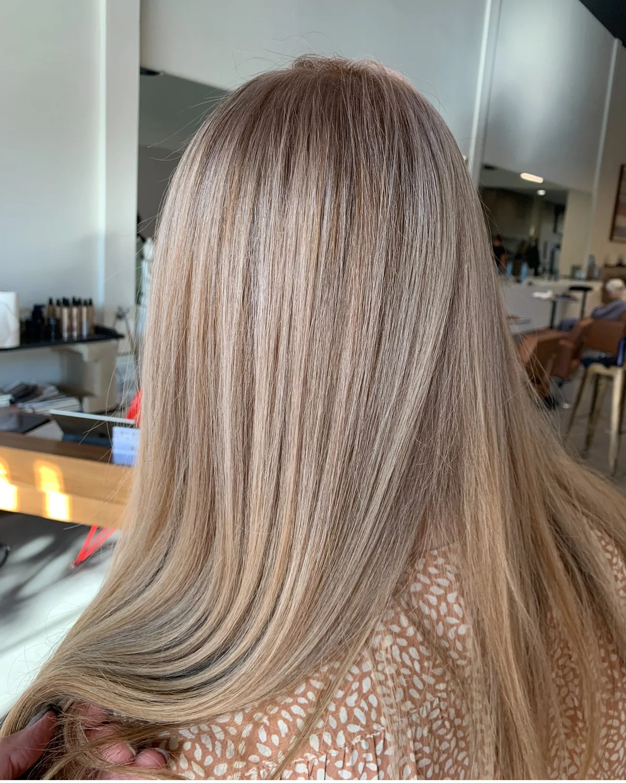 Back of a person's head with long, straight blonde hair in a salon setting.