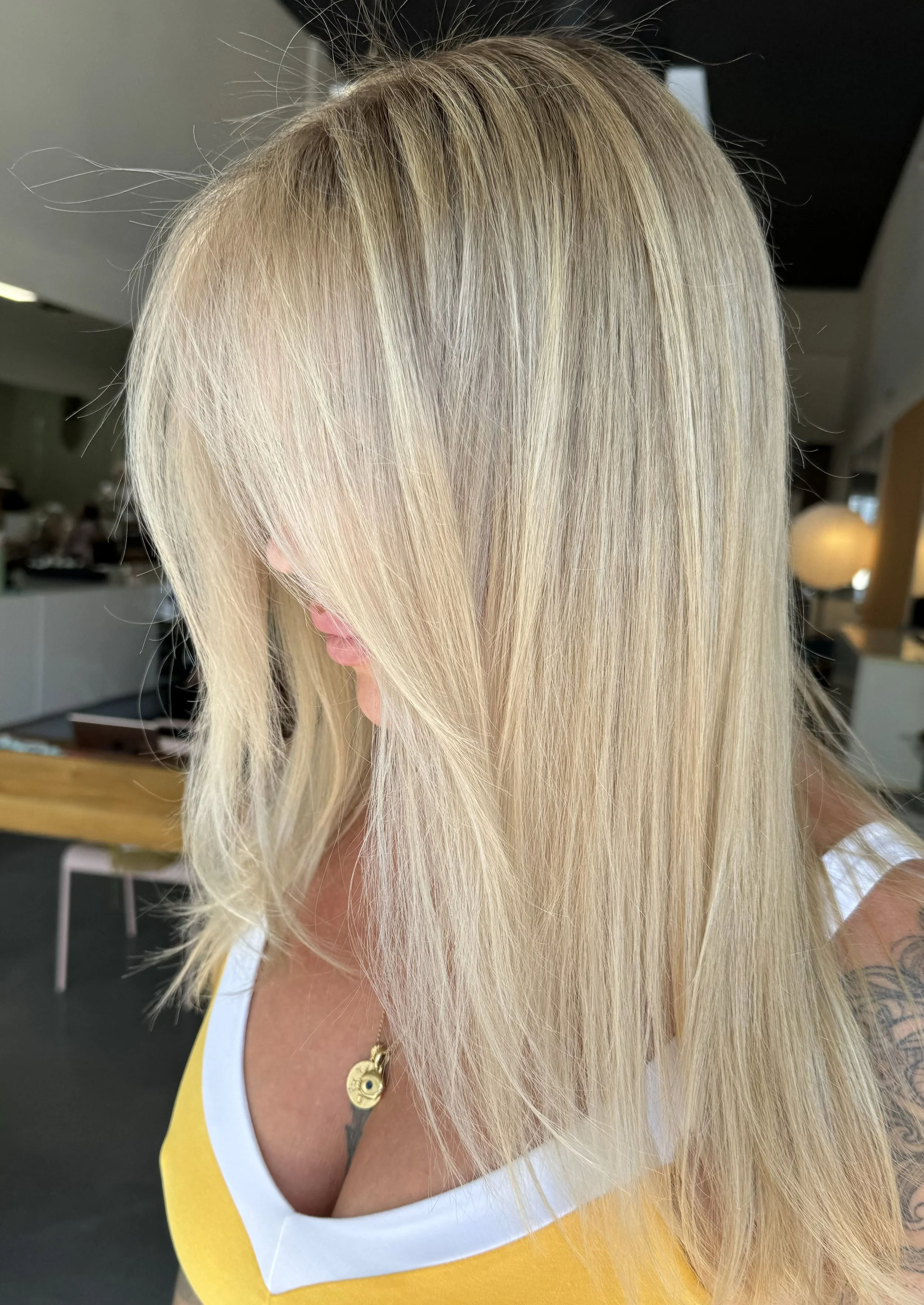 Woman with blonde hair and a tattoo sleeve on her arm in a yellow and white top, posing indoors.