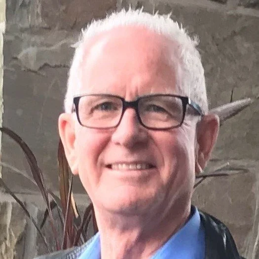 Close-up of a middle-aged man, smiling outdoors.