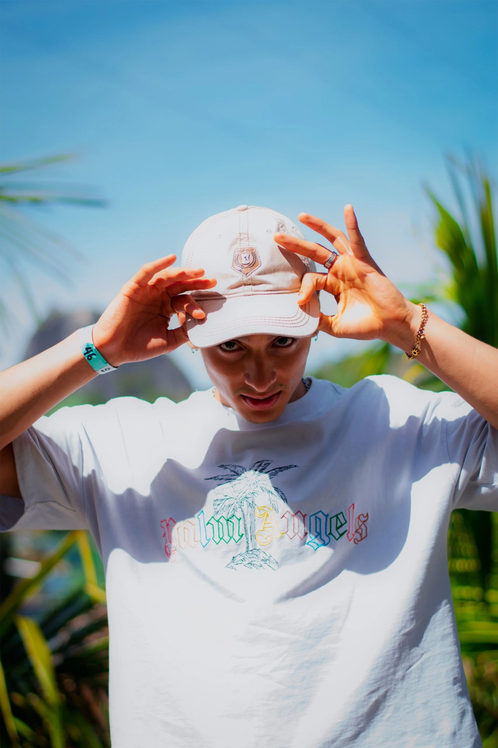 Joven ajustándose una gorra blanca en un entorno al aire libre con vegetación y cielo azul
