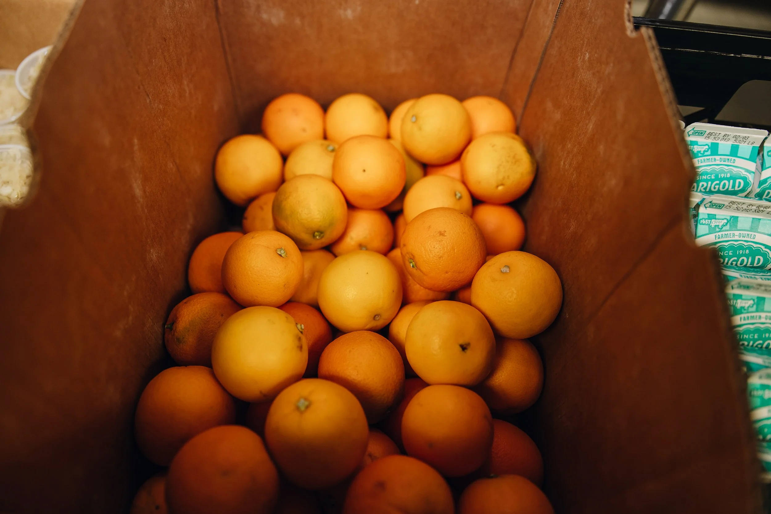 A box filled with yellow and orange grapefruits, some with small blemishes, inside a grocery store.