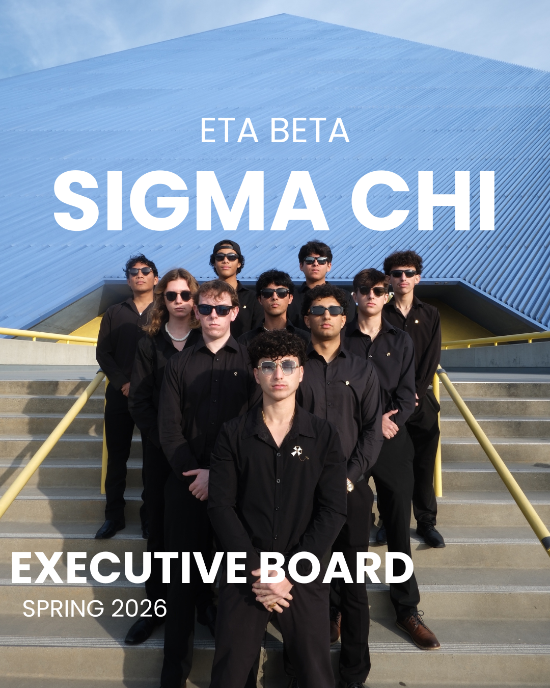 Group of young men standing on stairs outside of a modern blue building, wearing black clothing and sunglasses, with text overlay that reads 'ETA BETA SIGMA CHI EXECUTIVE BOARD SPRING 2026.'