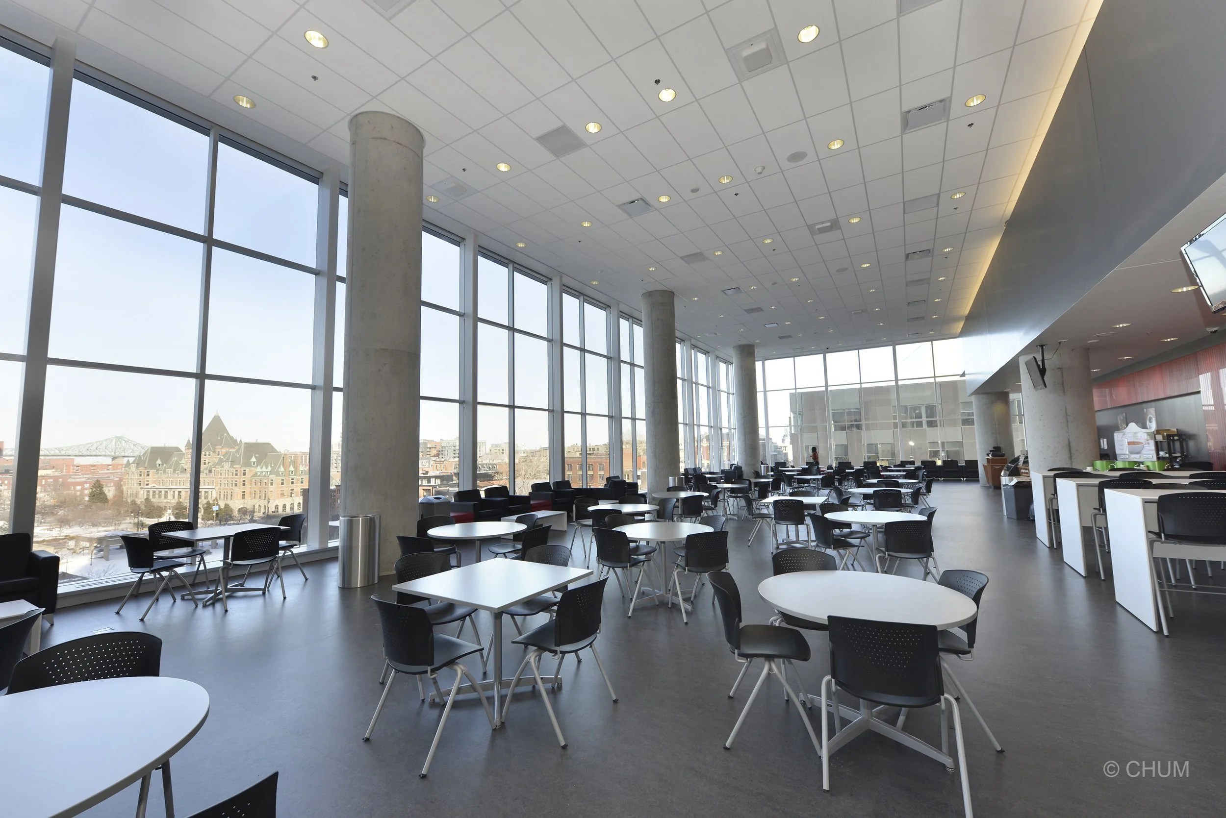 Modern airport lounge with large windows, round tables, black chairs, and cityscape view outside