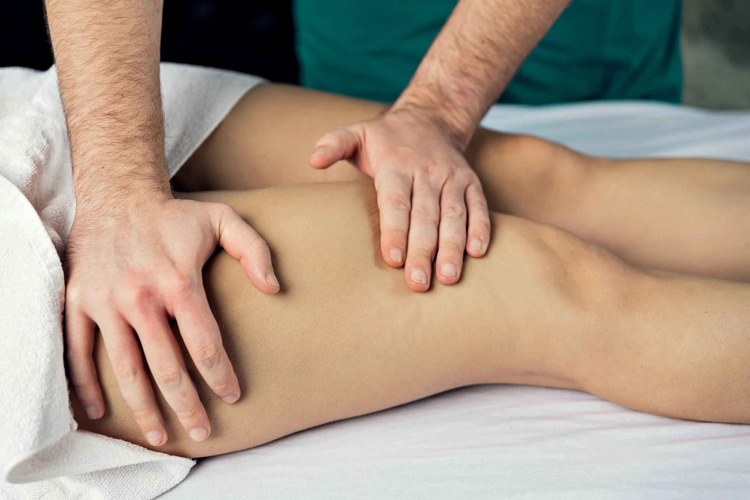 A massage therapist uses their hands to perform a massage on a person's thigh and leg.
