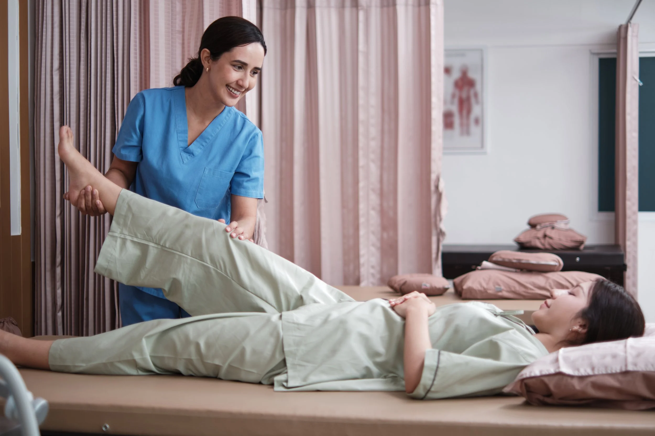 Nurse or caregiver assisting a patient to stretch or move her leg in a medical setting.