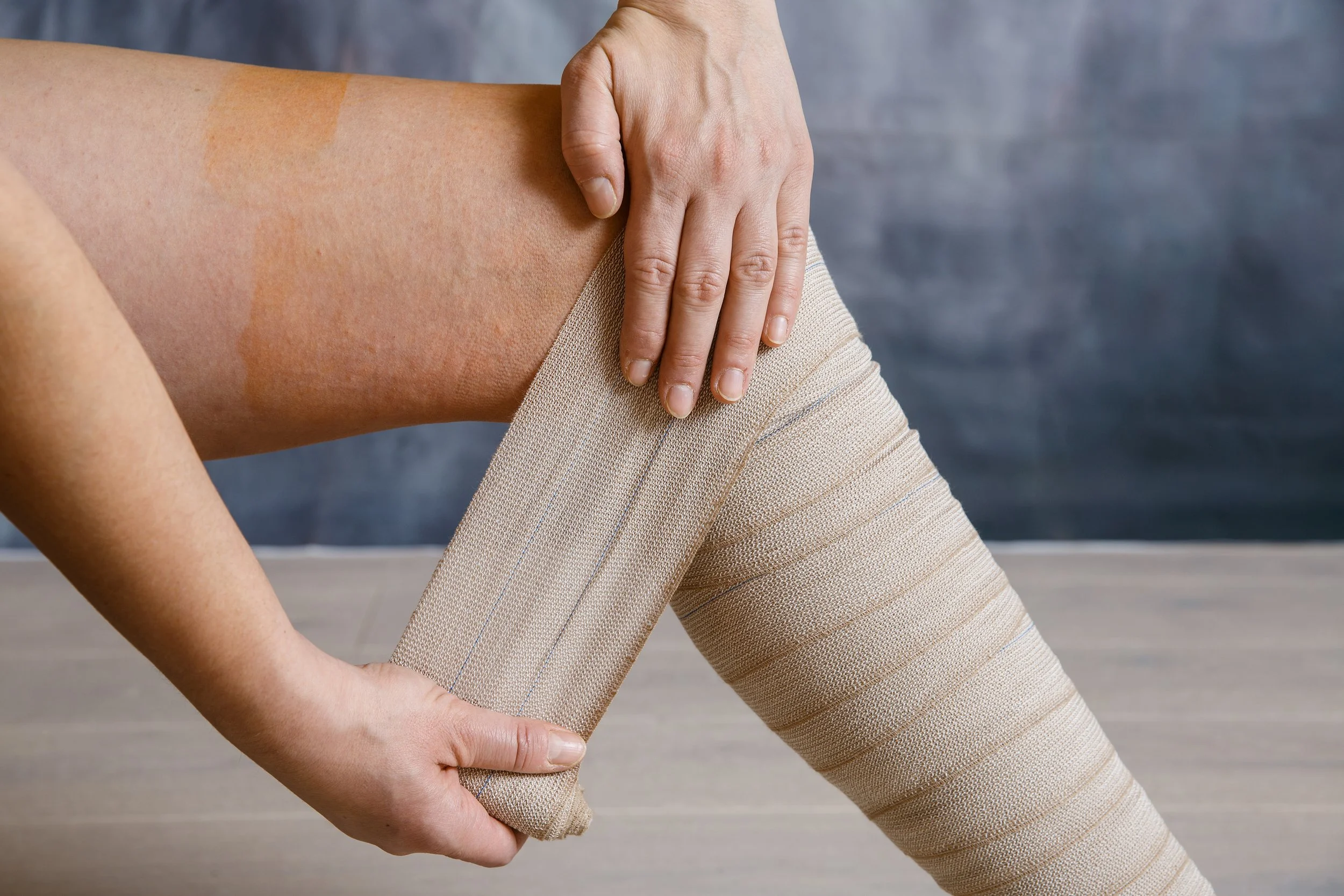 Person wrapping a beige compression bandage around their leg for lymphatic compression support.