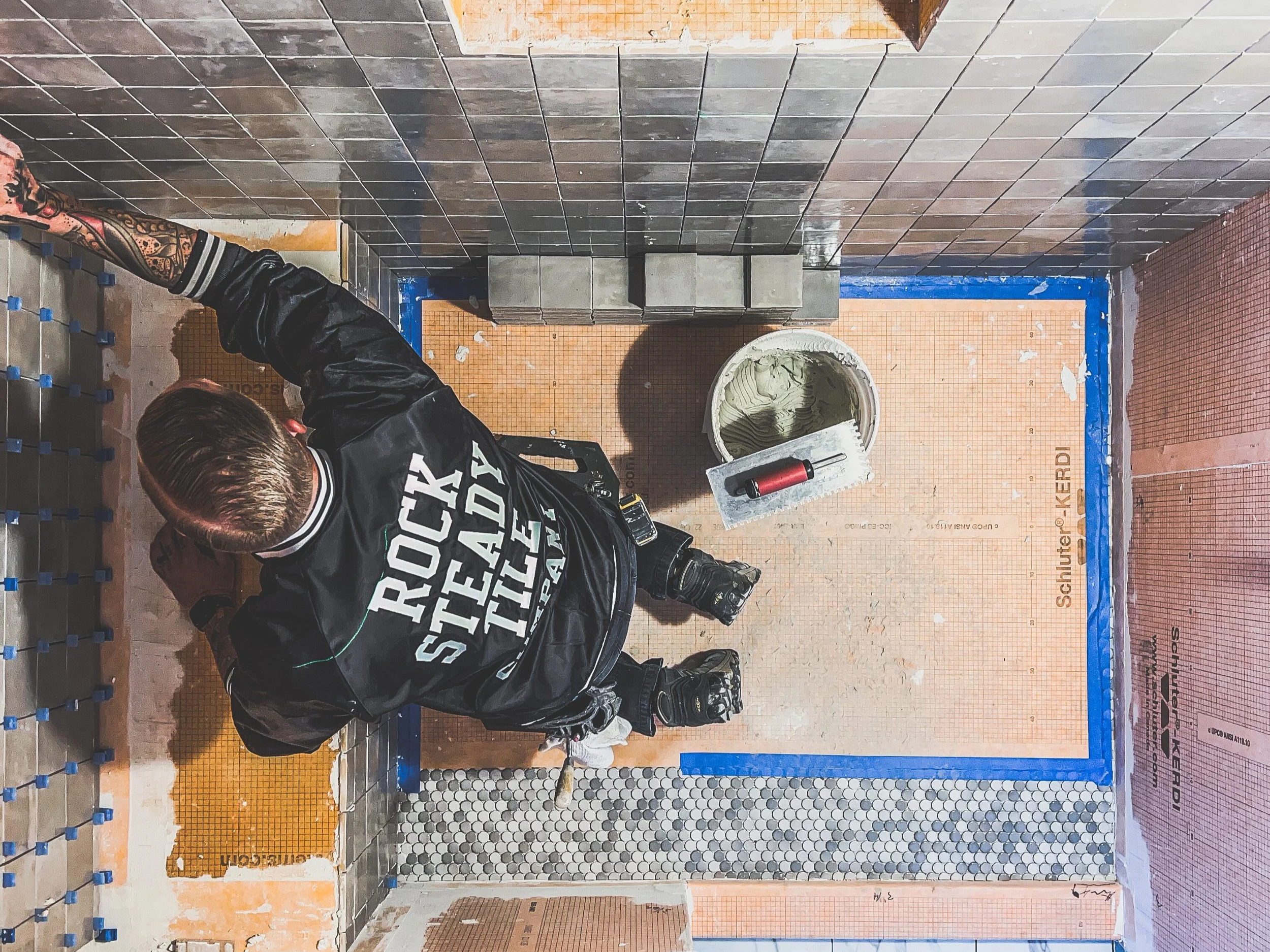 A worker installing tile on a wall in a bathroom, with various tools and materials around him.