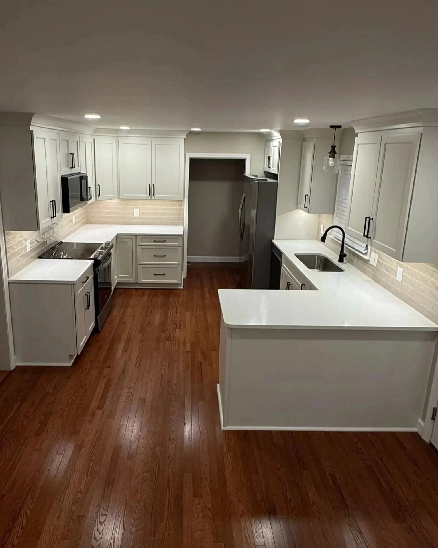 Kitchen with white cabinets, wood flooring, gray appliances, white countertops, and a tiled backsplash.