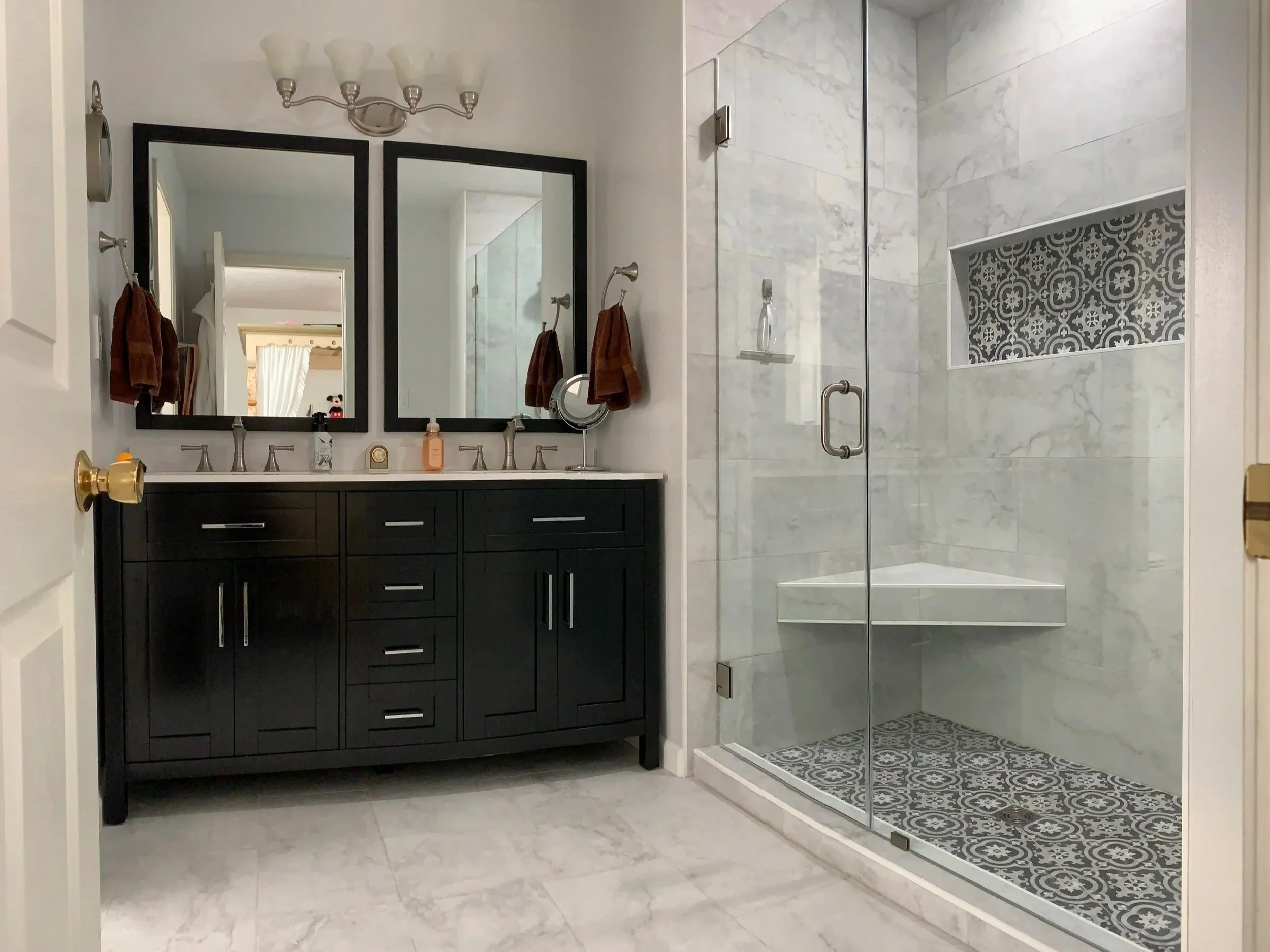 Modern bathroom with a black double vanity, two mirrors, and a glass-enclosed shower with patterned tiles.