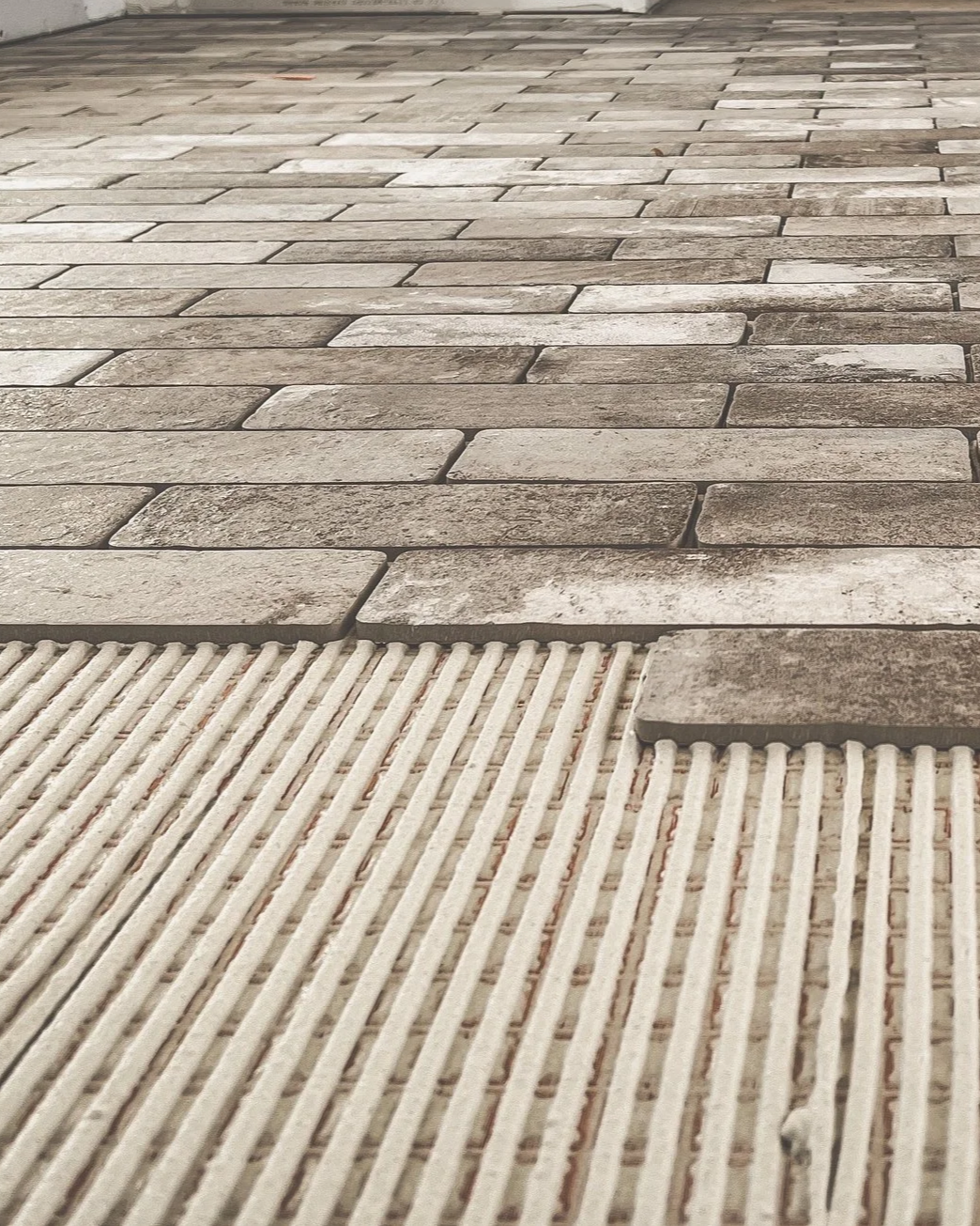 Close-up of a tiled brick floor with a section of textured concrete or rubber matting at the bottom.