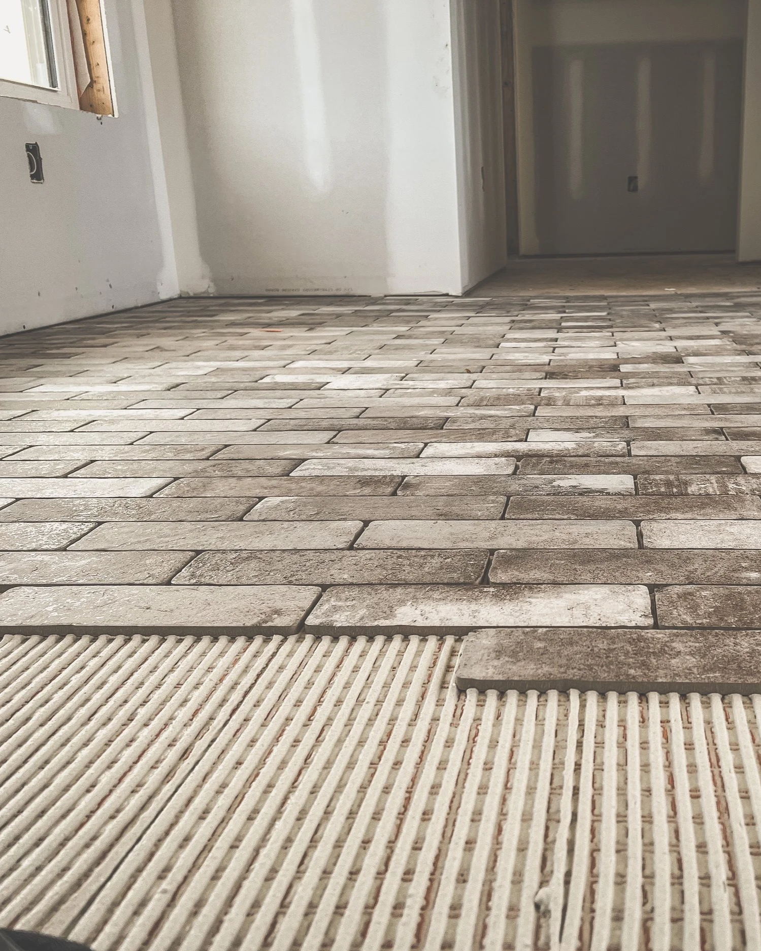 Interior room with brick pattern wooden flooring and a built-in floor vent, under construction or renovation.