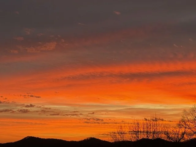 Colorful sunset sky with orange and yellow hues over a silhouette of trees and hills.