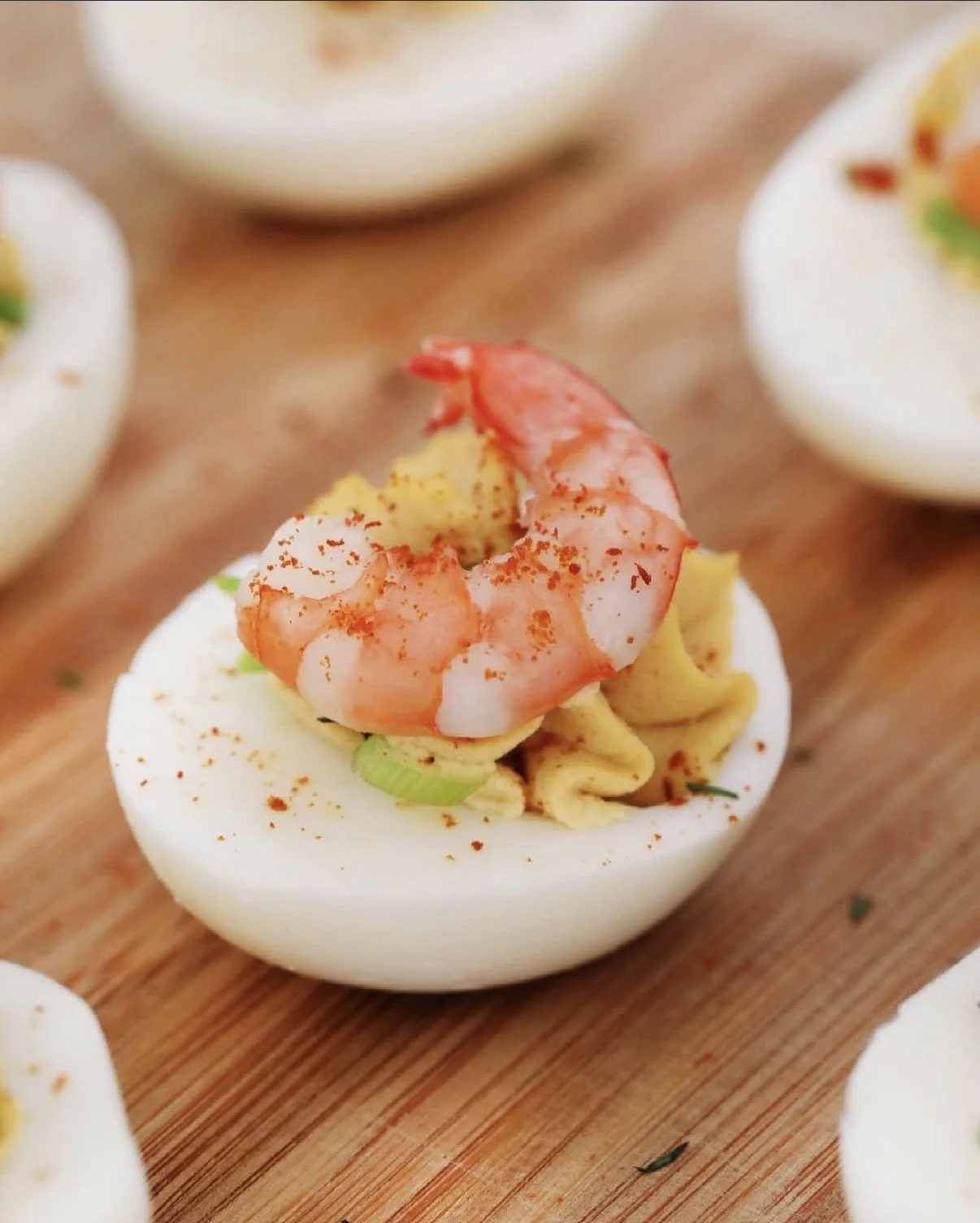 Deviled eggs topped with shrimp, paprika, and chopped green onions on a wooden platter.