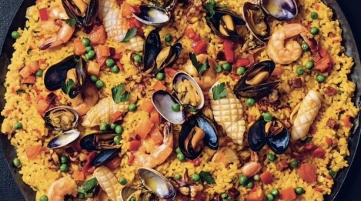 Seafood paella with shrimp, mussels, squid, peas, and diced vegetables on a large black serving platter.