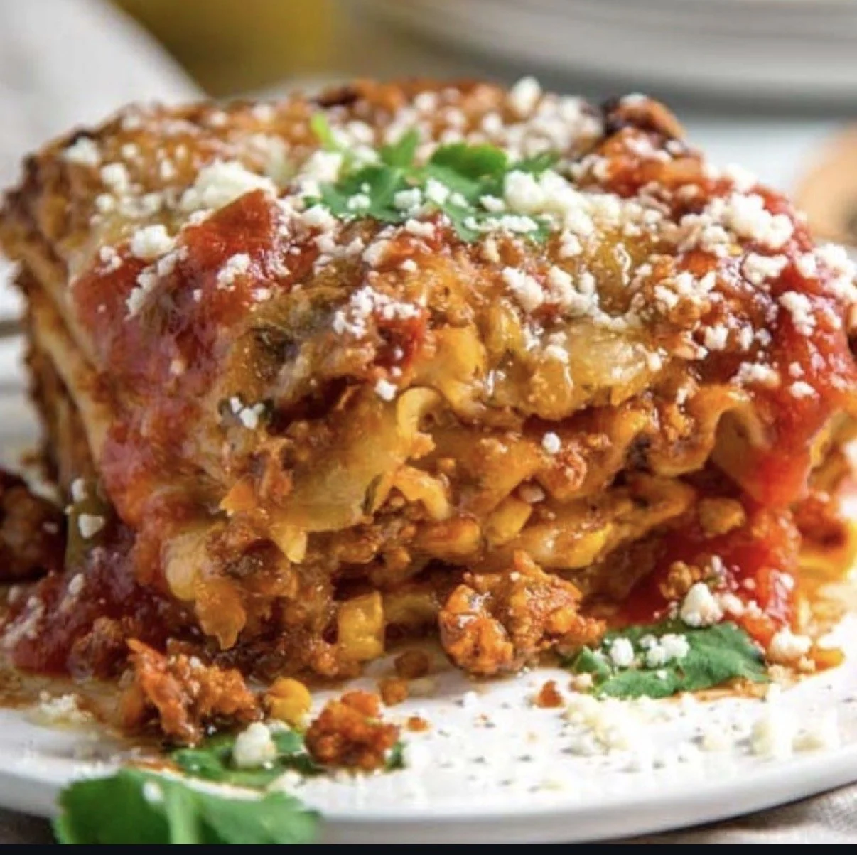 A close-up of a serving of layered Mexican baked casserole with melted cheese, tomato sauce, ground meat, and garnished with fresh cilantro and crumbled cheese on top.