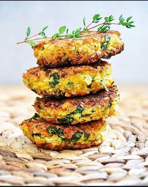 Stack of four vegan chickpea and spinach veggie patties garnished with a sprig of thyme on top, placed on a woven mat.