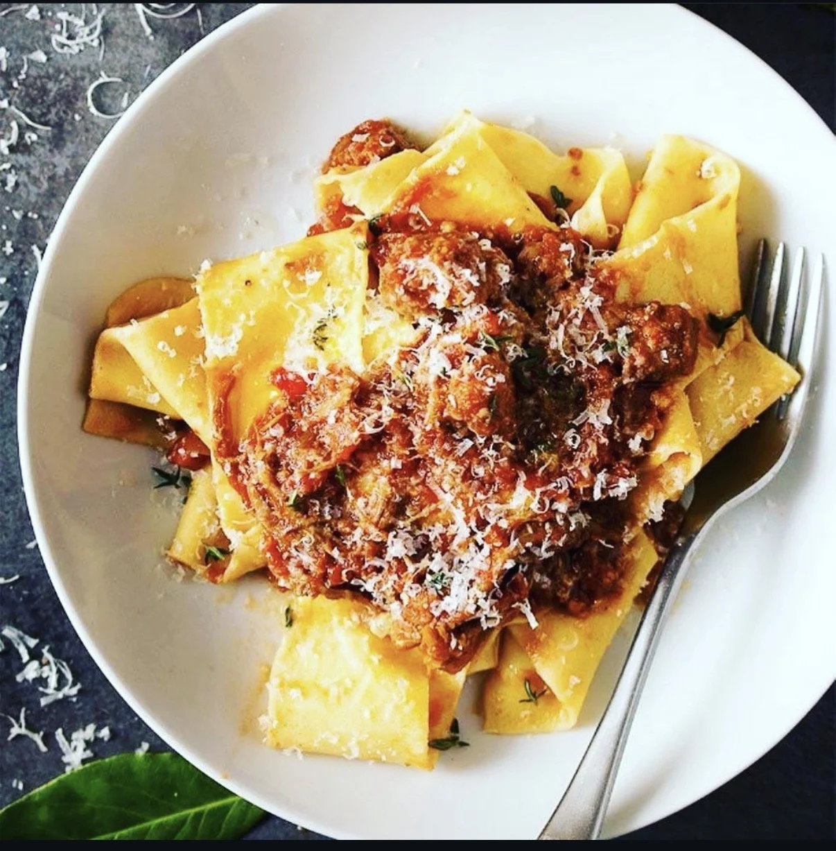 Plate of cooked pasta with meat sauce, topped with grated cheese.