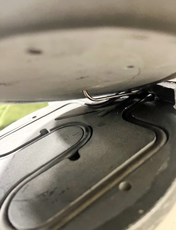 Close-up of a frying pan on a stove with a small metal paperclip inside, partially visible from underneath.