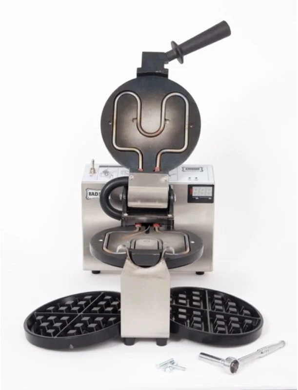 A commercial waffle maker with a flip lid, digital control panel, and a round cooking surface, placed on a white background with accessories including a batter paddle and screws.