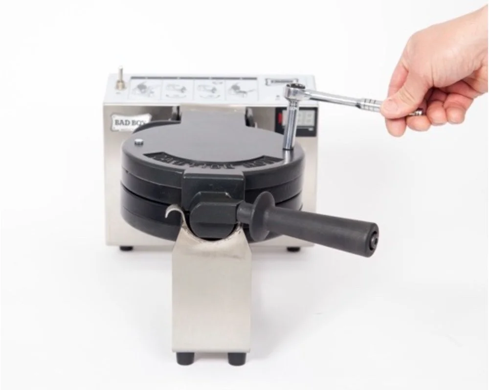 A person using a ratchet wrench to open or close a circular black device on a silver machine.