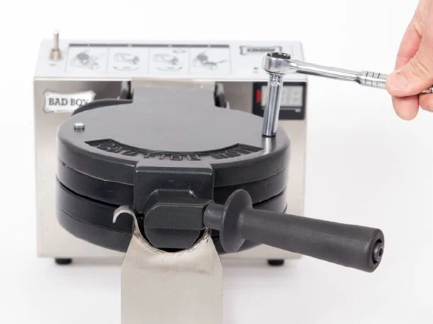 A person using a wrench to open a black circular device, with a white labeled box in the background.