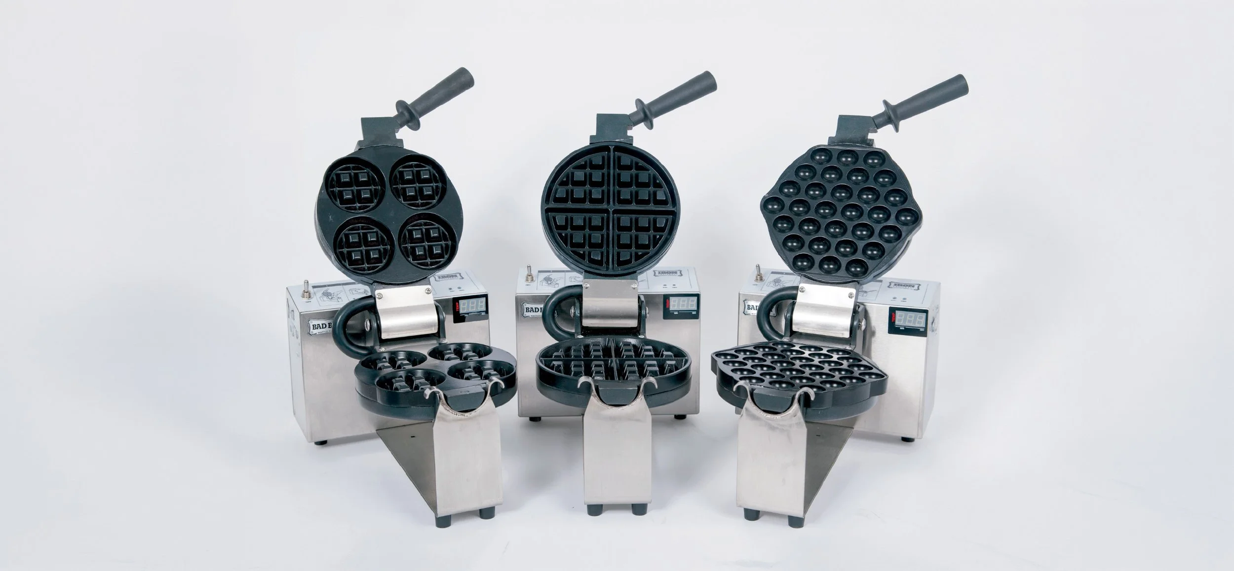 Three commercial waffle makers with open lids, each with a different pattern of waffle plates, against a plain white background.