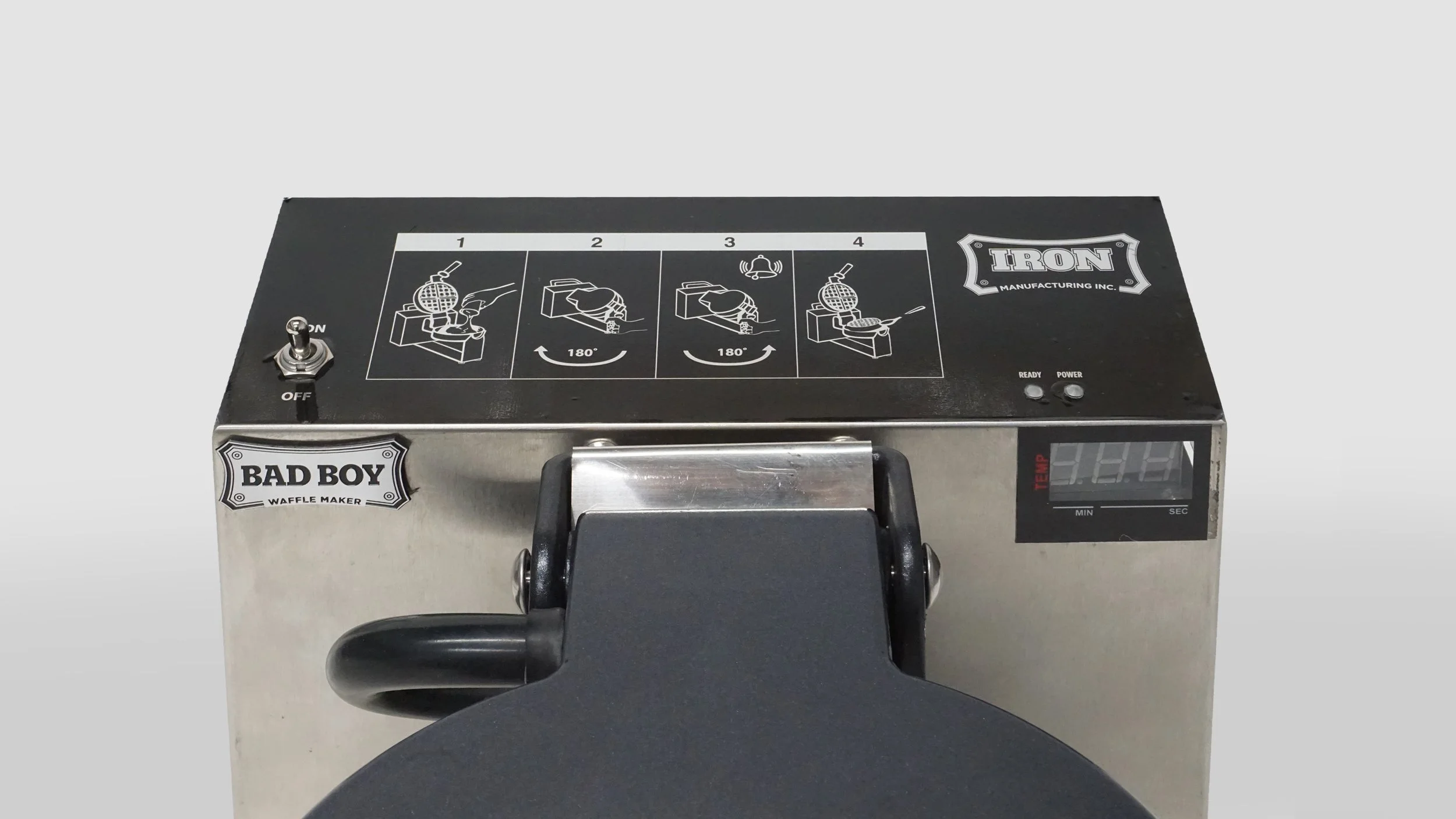 Stainless steel waffle iron with black controls and a digital thermometer, labeled 'BAD BOY' Waffle Maker, with instructions and a switch on top.