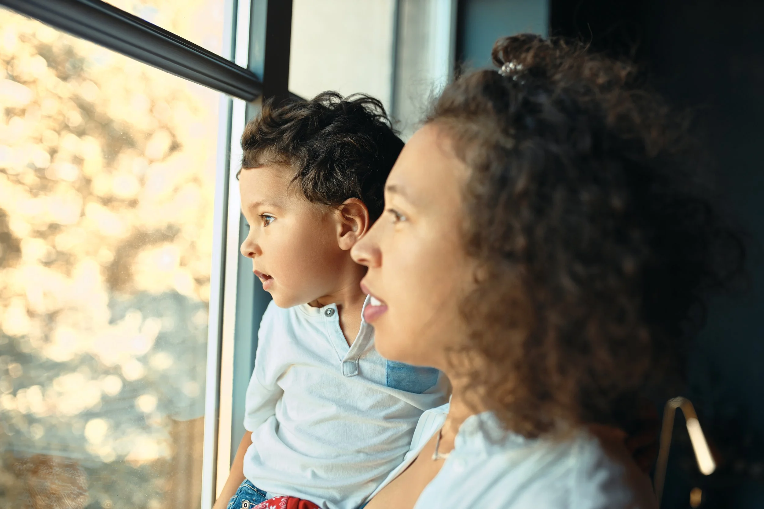 A woman and a young boy looking outside a window with curious expressions.