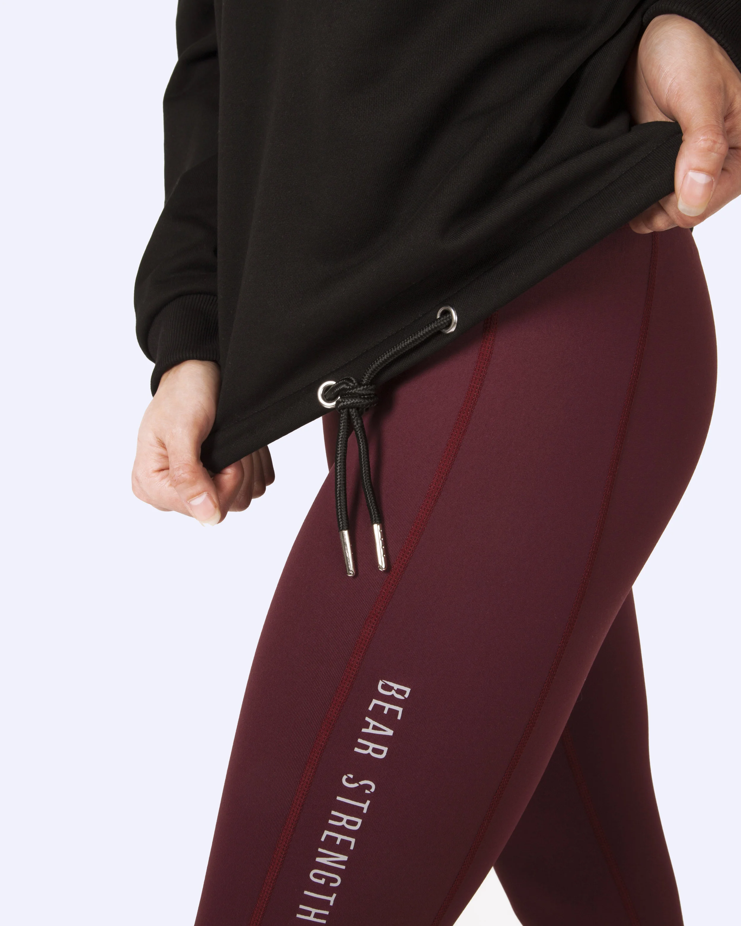 Close-up of a person wearing red leggings with white text reading 'BEAR STRENGTH' and a black jacket.