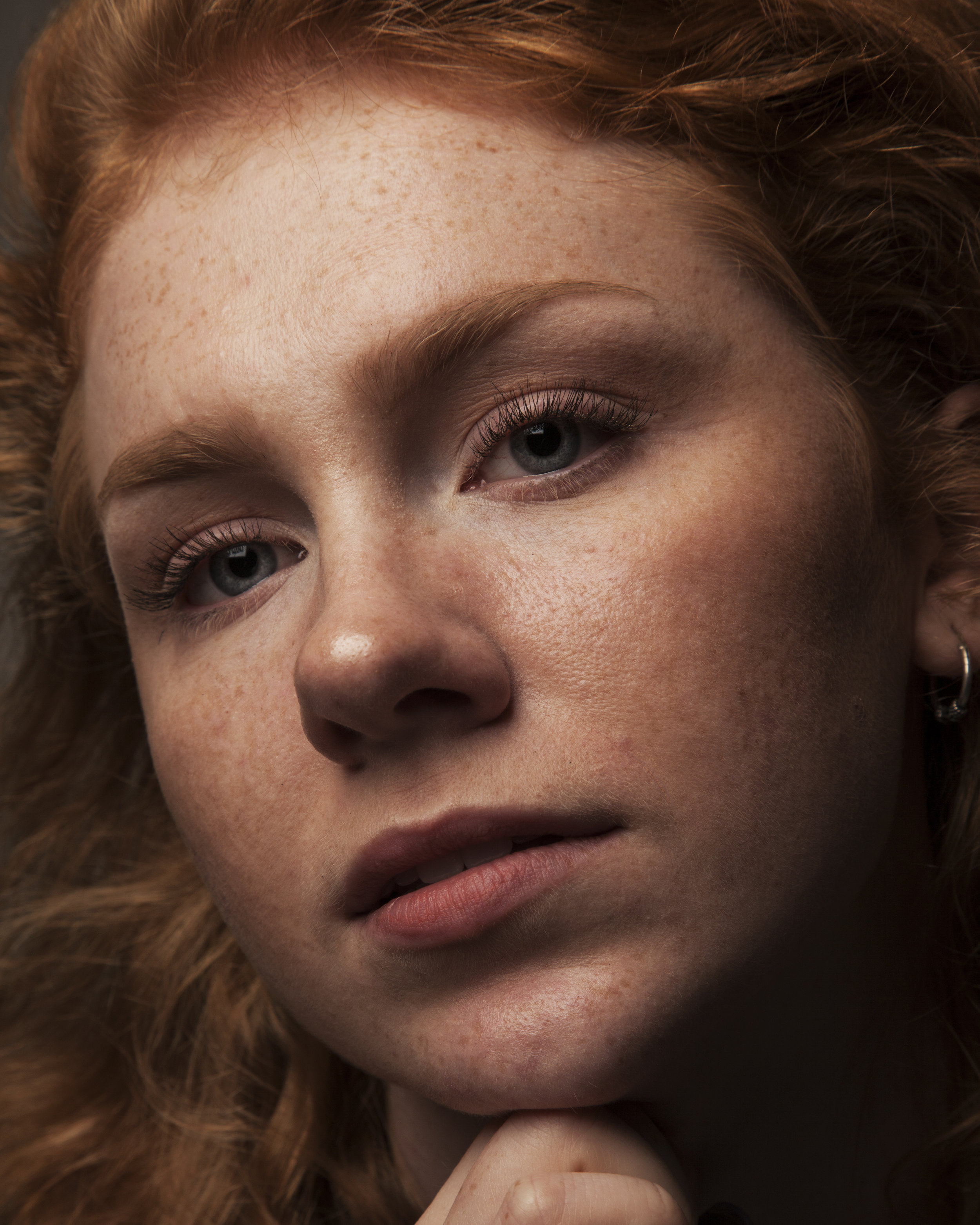 Close-up of a young woman with curly red hair, freckles, and blue eyes, resting her chin on her hand.