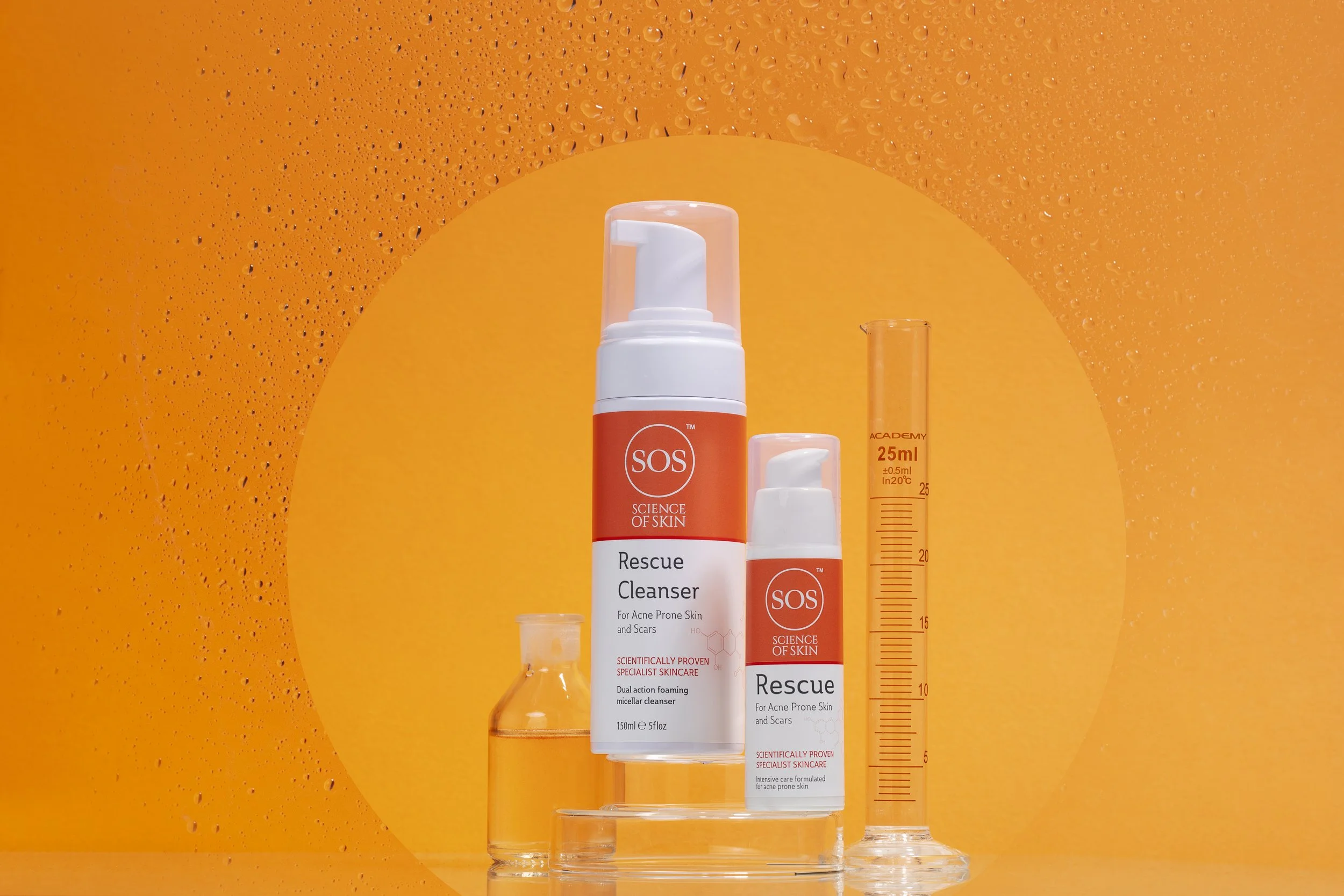 Skincare products, including SOS Rescue Cleanser and Rescue Serum, with measuring beakers and a yellow-orange background.
