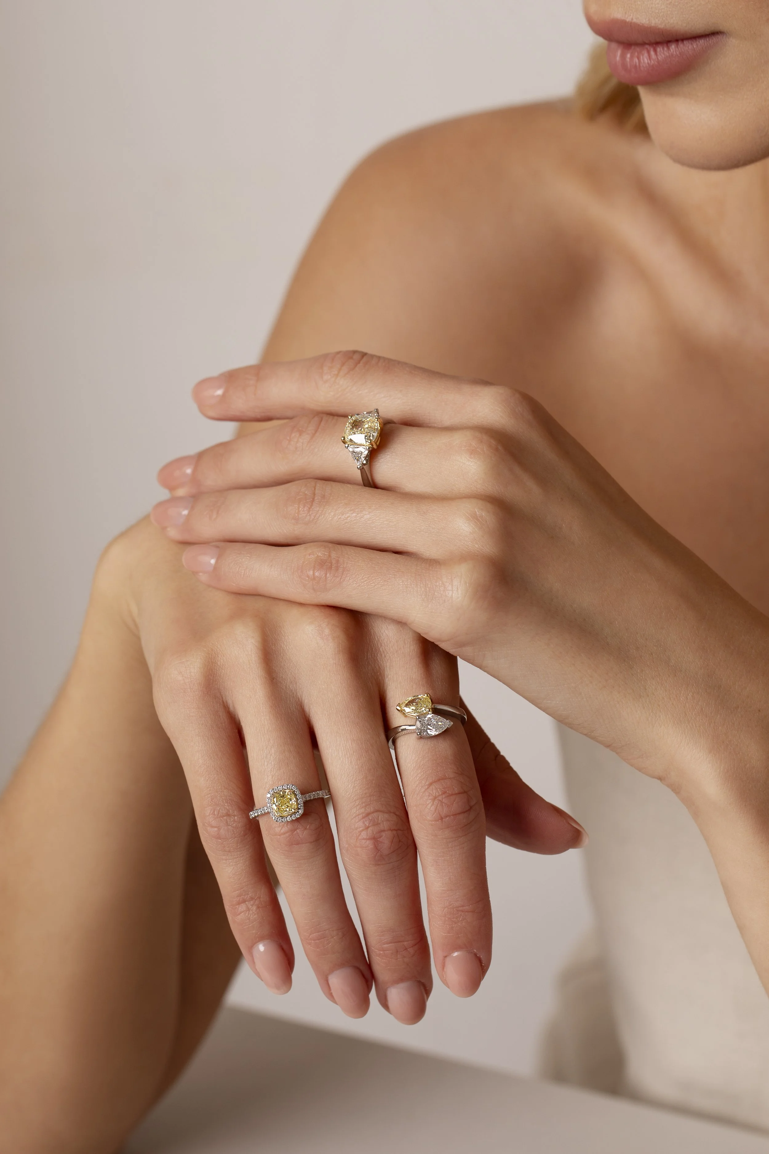 Close-up of a woman’s hands showing rings with yellow, white, and clear gemstones, with part of her face and shoulder visible.
