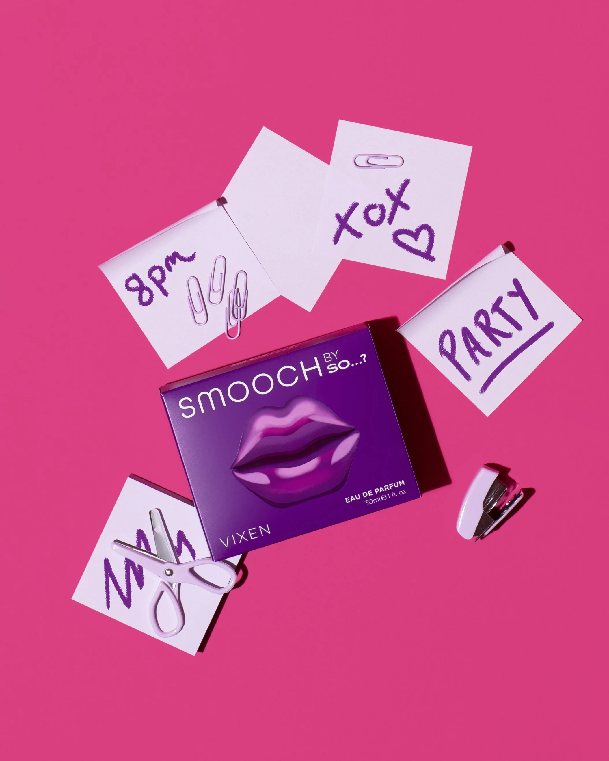 A pink background with a purple box of 'smooch' perfume, two paper notes with '8 pm', 'text', and 'party' written in purple, a pair of white scissors, and a small white clip.