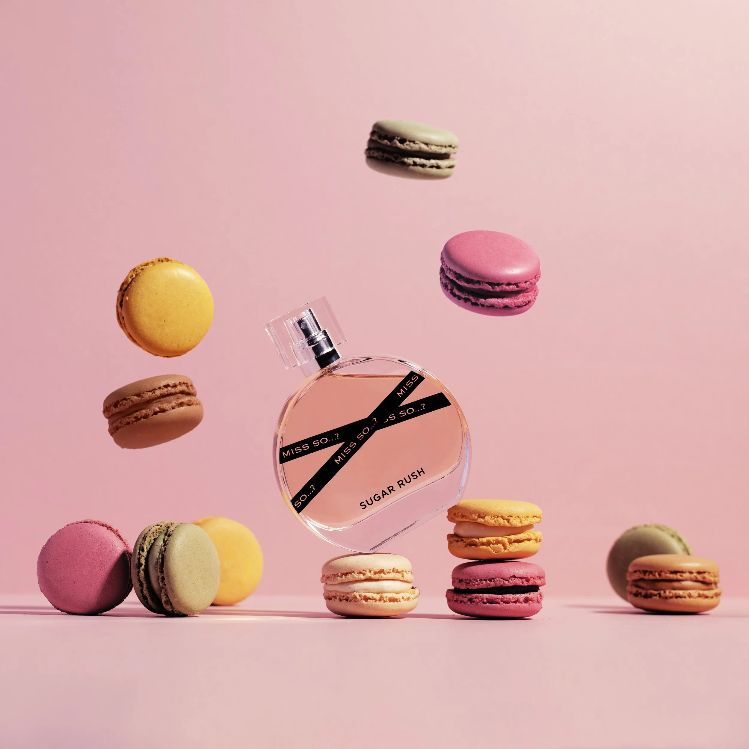 A bottle of Miss So...? Sugar Rush perfume surrounded by colorful macarons on a pink background.