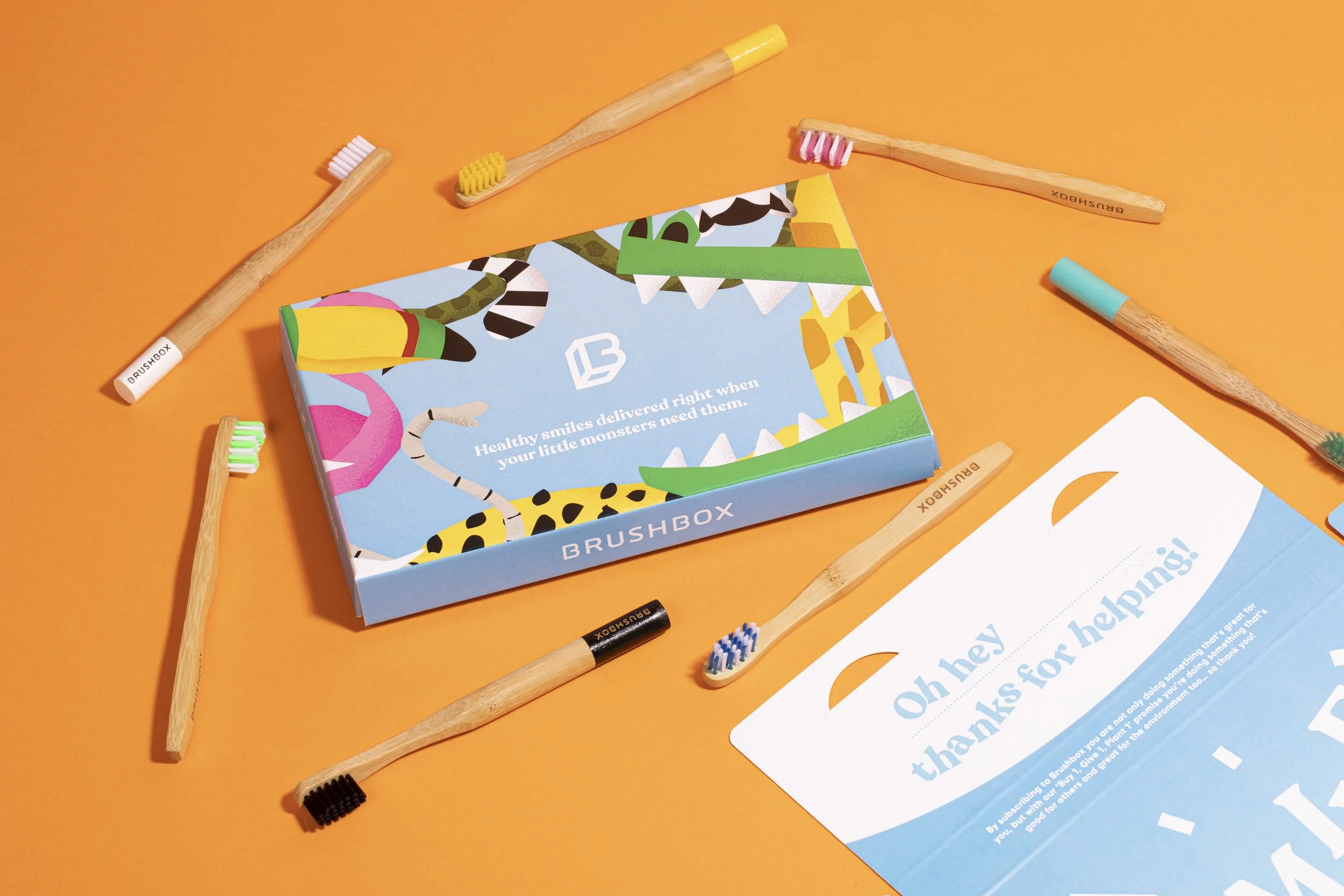 A colorful box of toothbrushes with a blue and green design, surrounded by several electric toothbrush heads on a bright orange background.