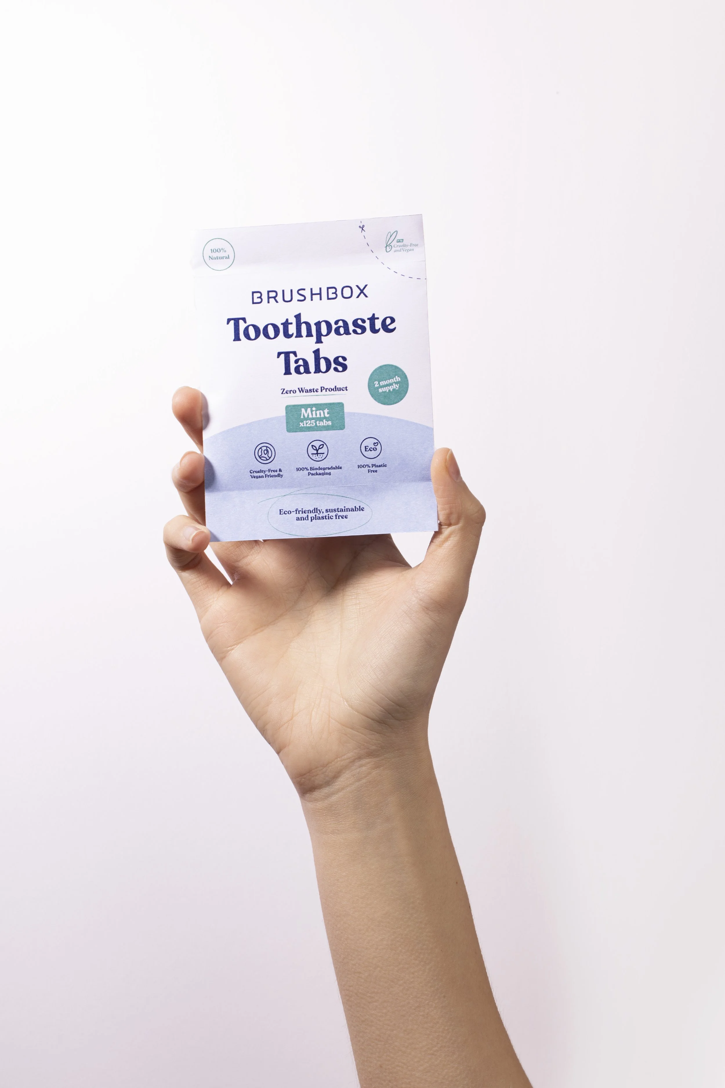 A hand holding a box of toothbrush toothpaste tabs with a white background.